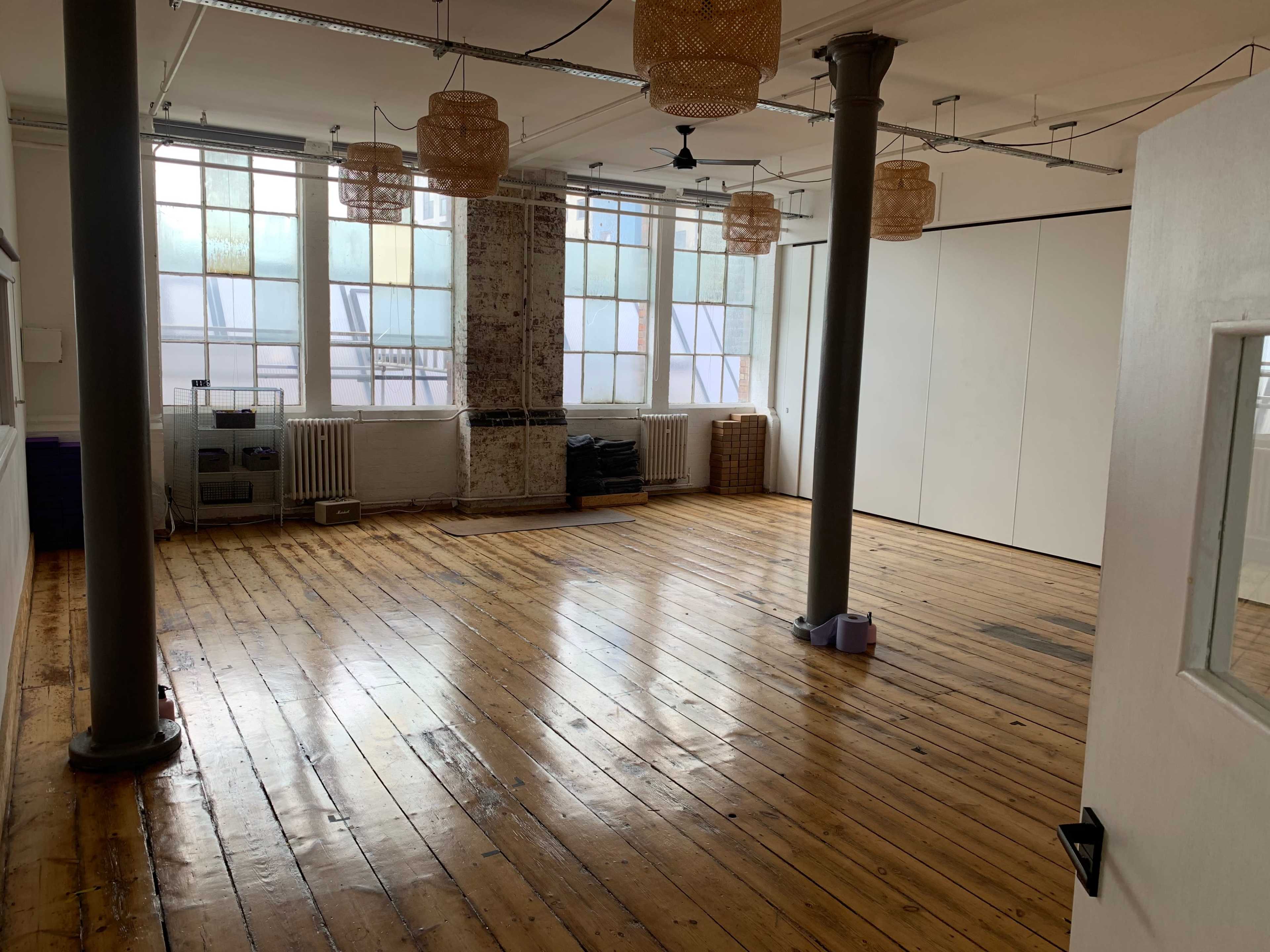 An empty studio space with wooden floors, large windows, and decorative light fixtures hanging from the ceiling.