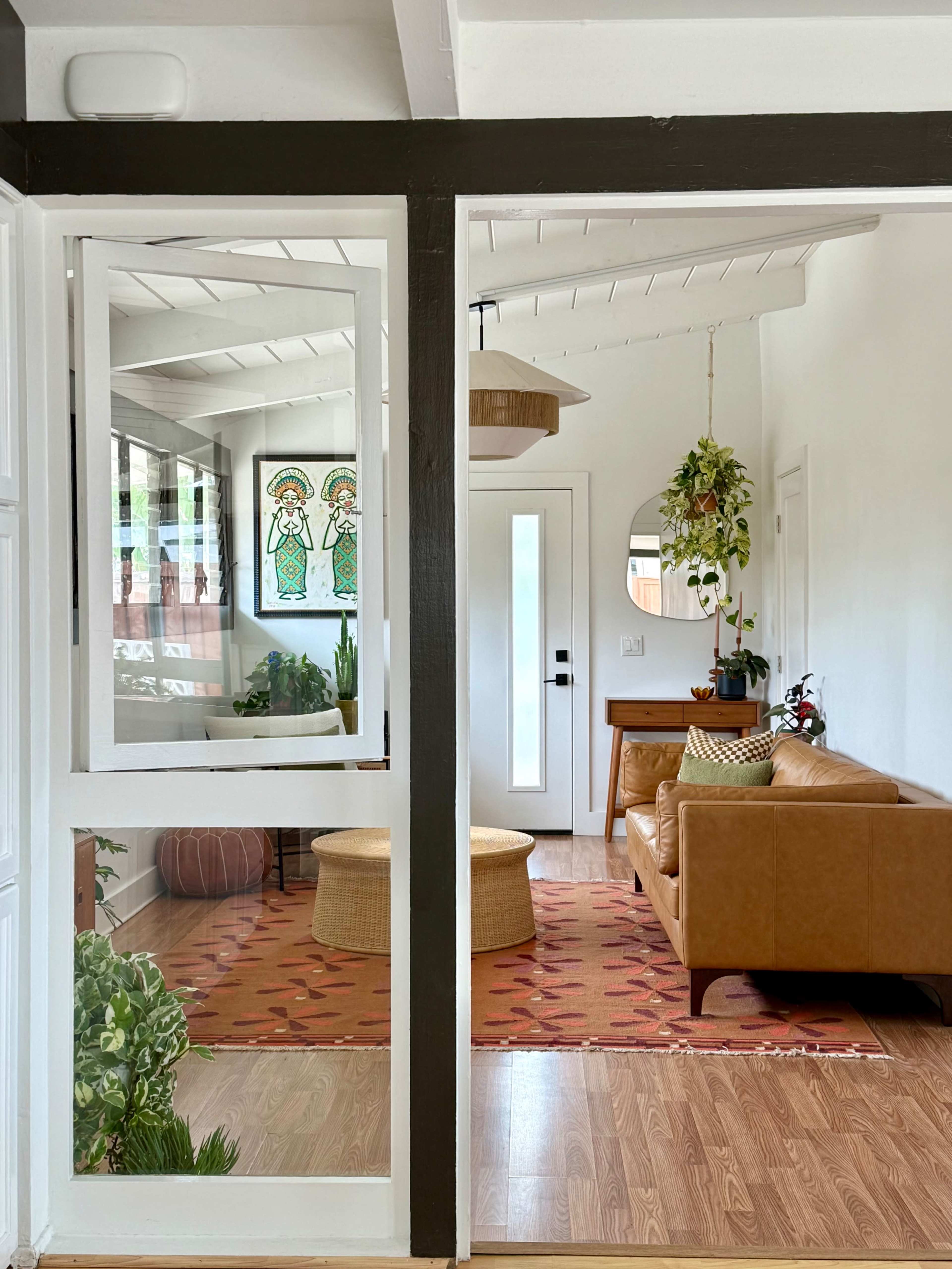 The image shows a warmly decorated living room with a brown leather sofa, a round woven coffee table, and a vibrant rug, visible through an open doorway framed by white and dark wood walls.