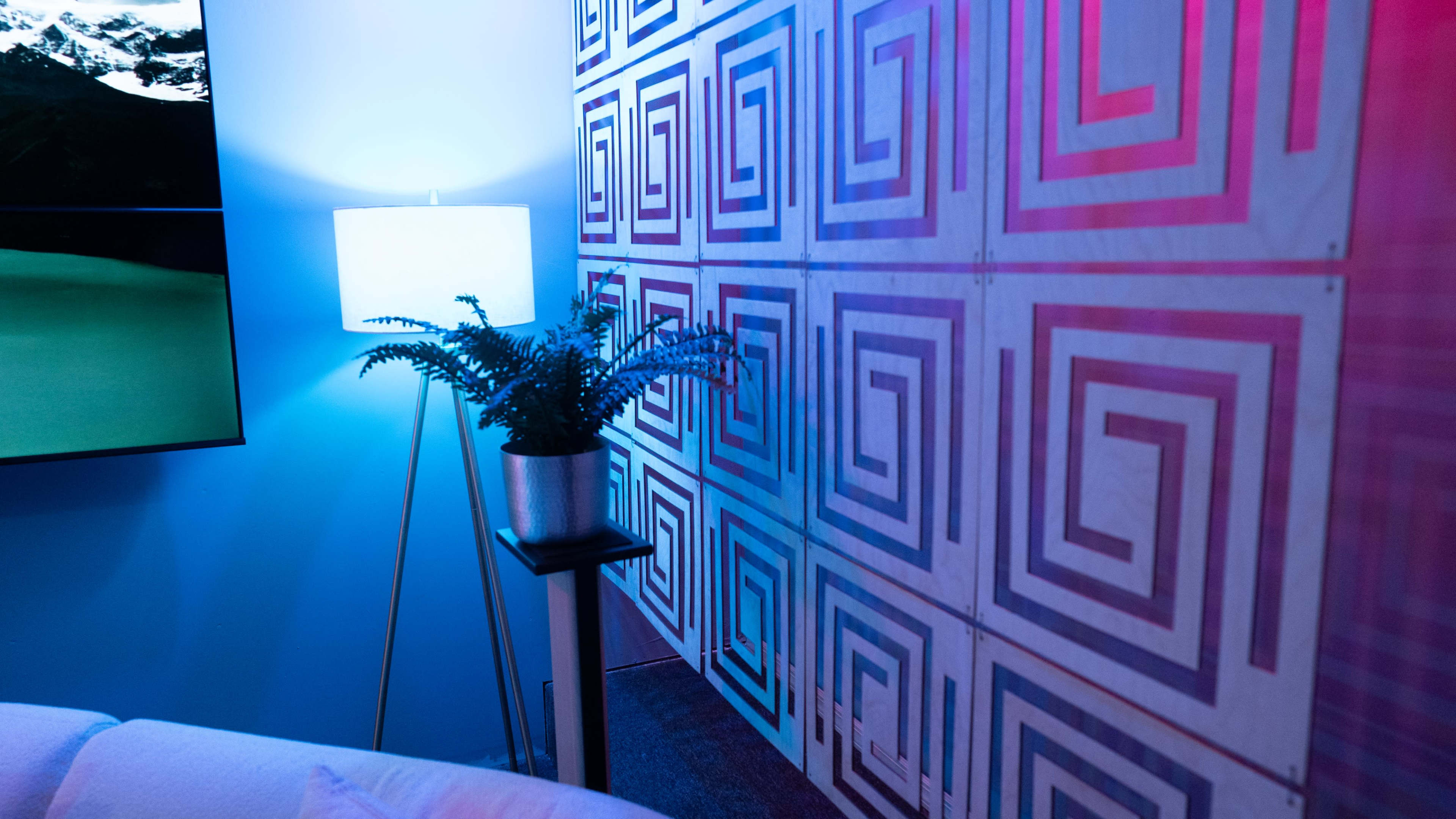 A corner of a room featuring a patterned wall, a floor lamp, and a potted plant on a stand.