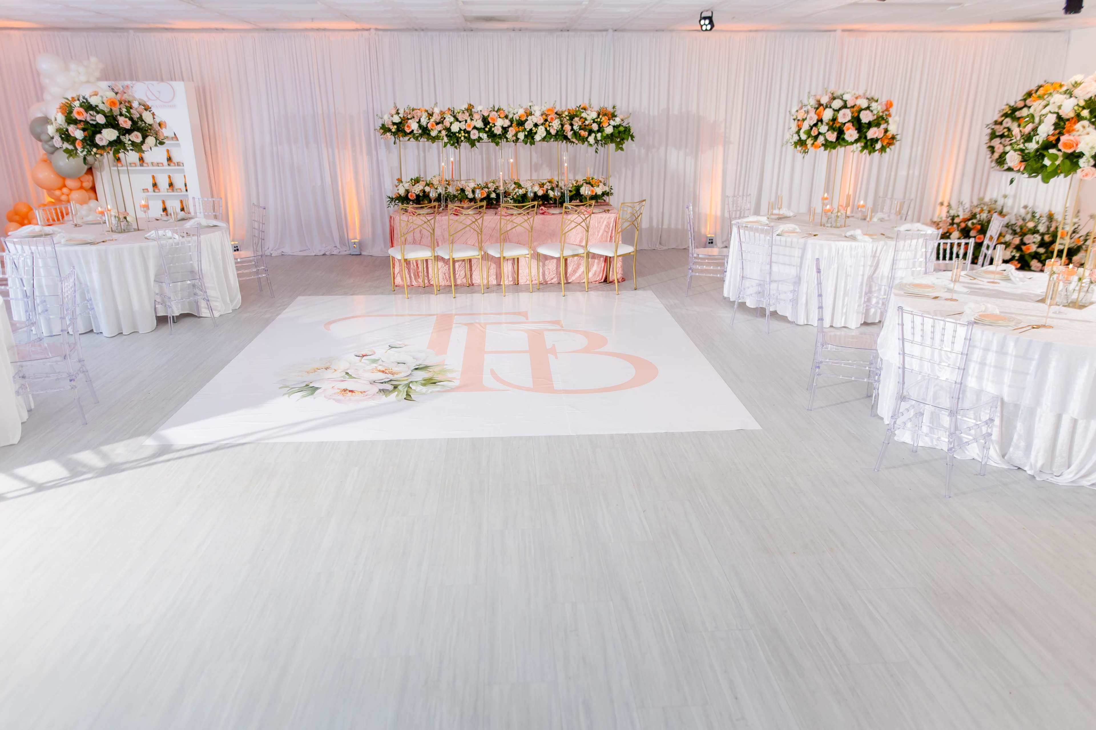 A decorated event space with floral centerpieces on tables and a large floral design on the floor featuring the letters "TB."