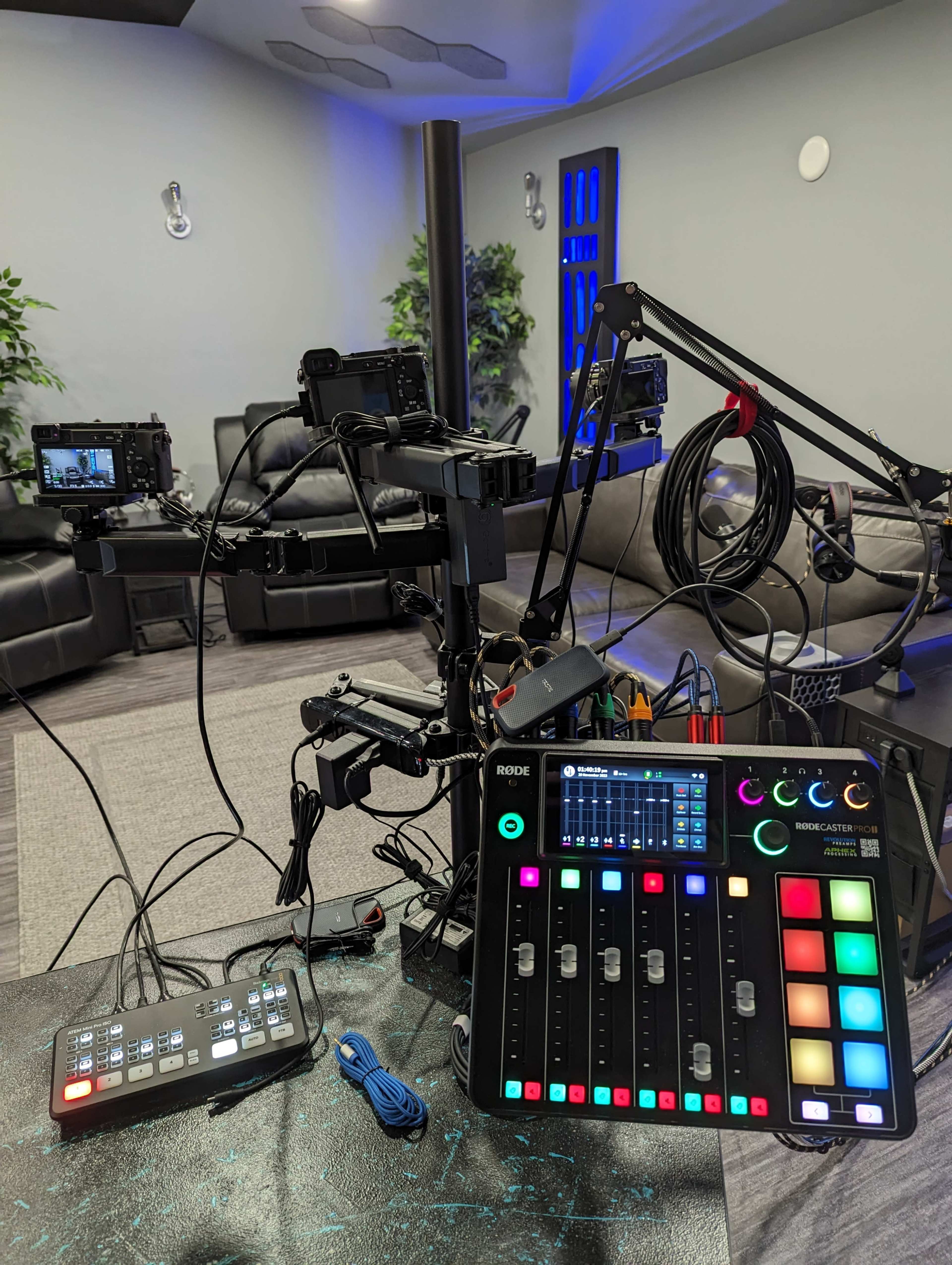 A multimedia setup featuring a Rodecaster Pro mixer, several cameras mounted on adjustable arms, and a modern seating area in the background.