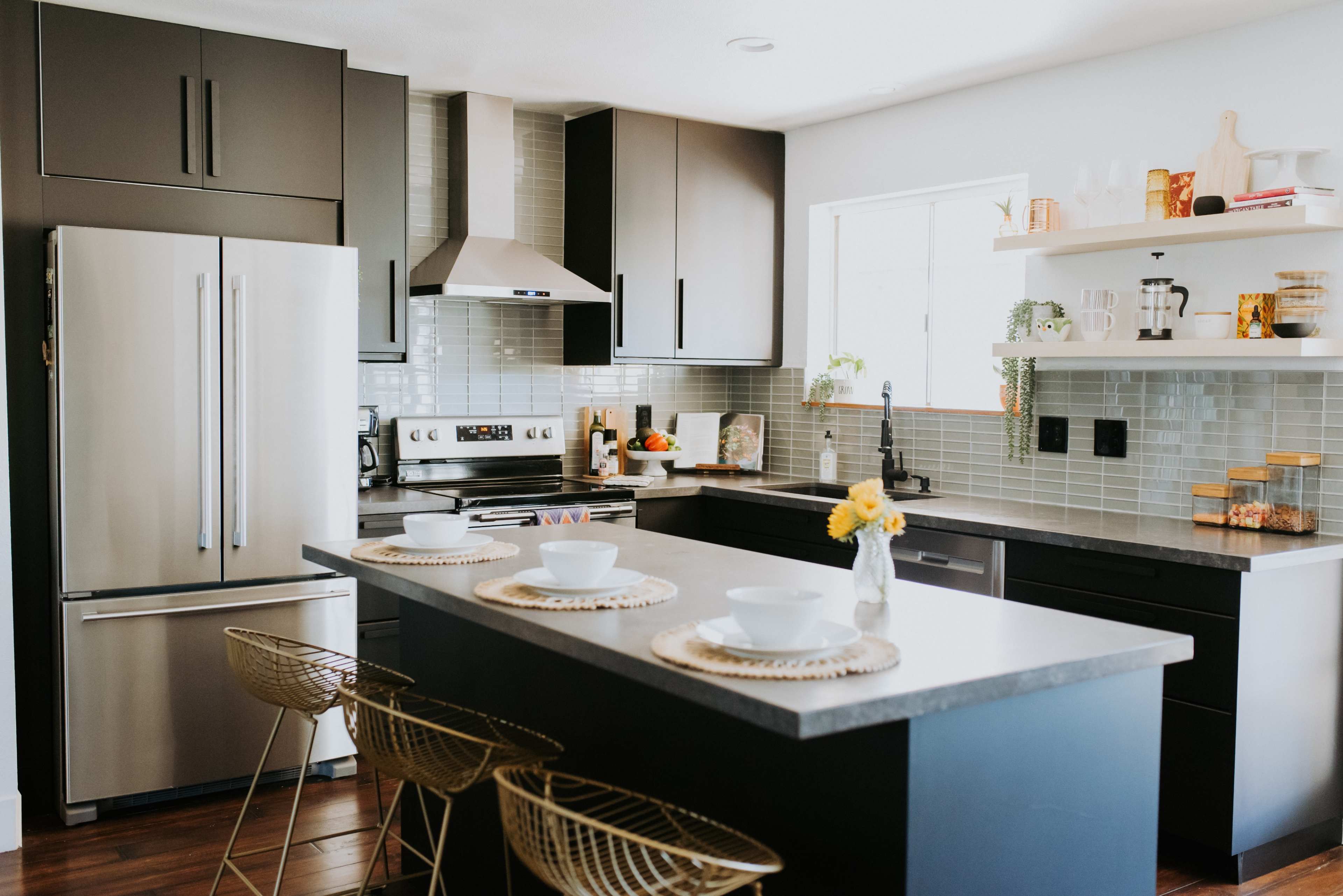 A modern kitchen features stainless steel appliances, a central island with stools, and open shelving displaying various kitchen items.
