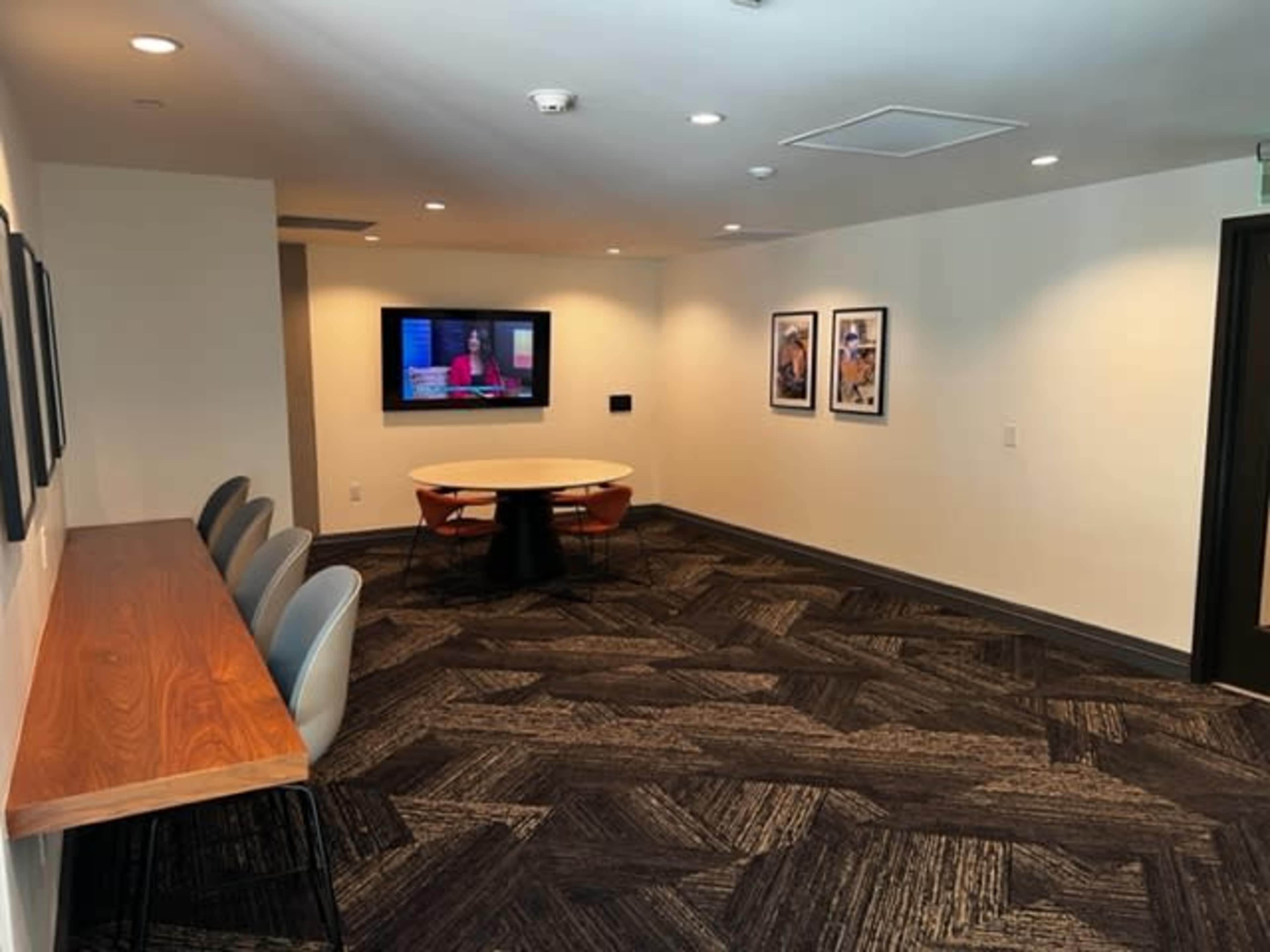 A modern meeting room featuring a circular table with chairs, a wall-mounted television, and framed pictures on the walls.