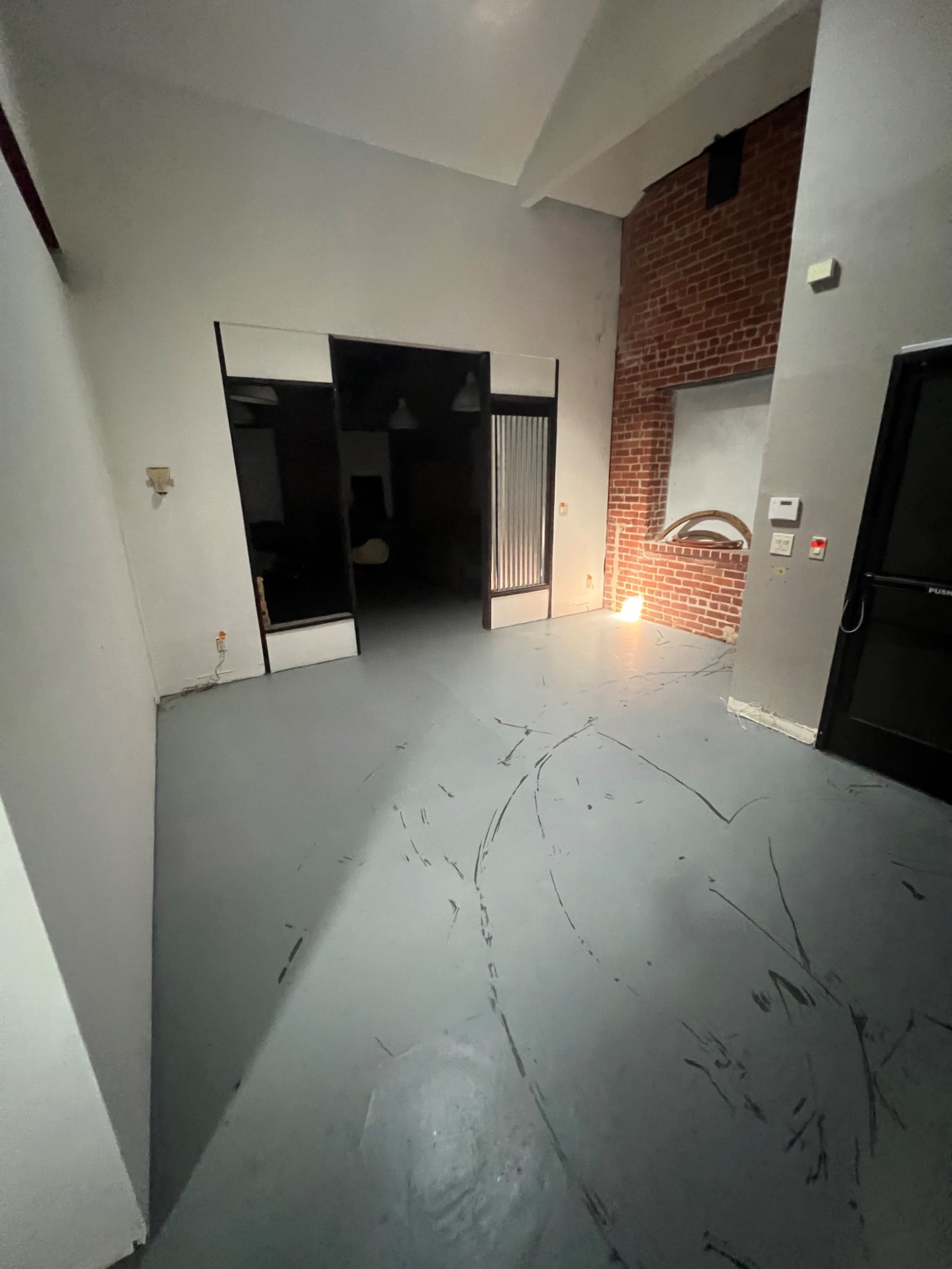 The image shows a spacious room with a gray floor, a brick wall, and two darkened doorways leading to separate areas.