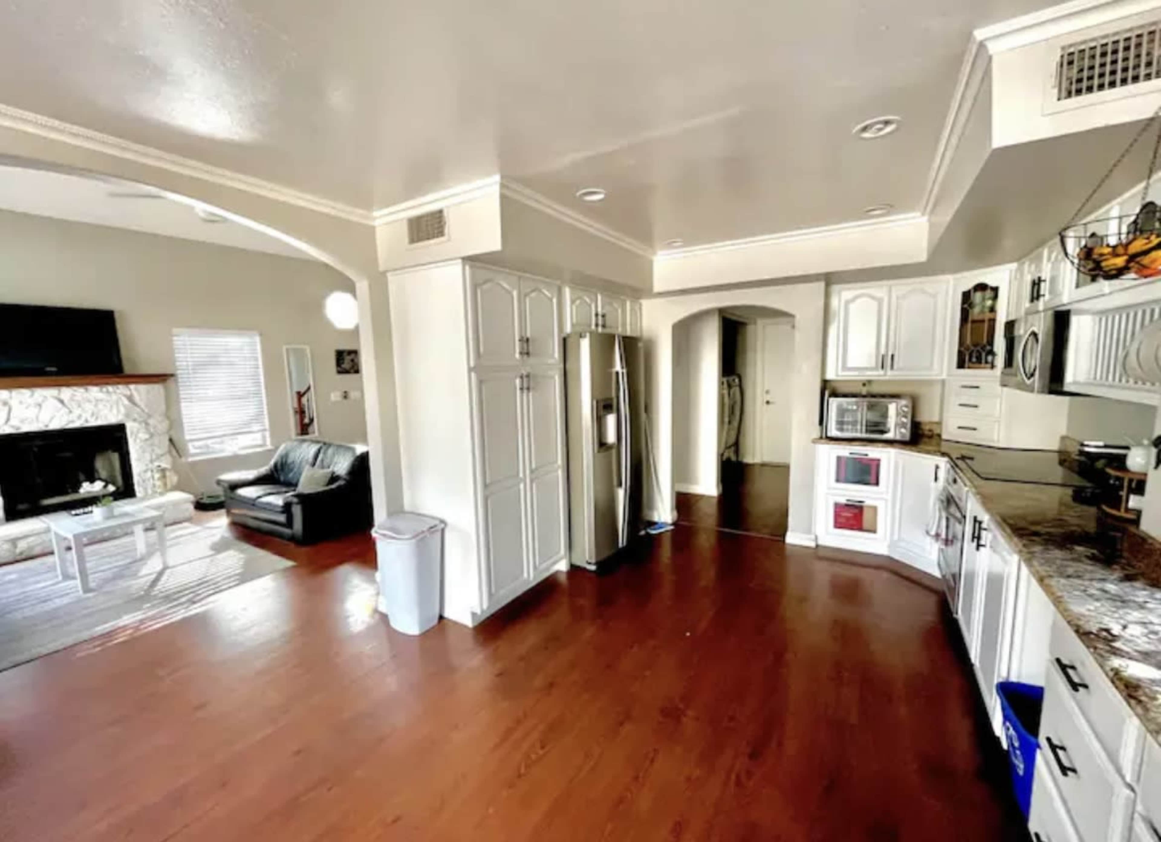 A spacious kitchen with white cabinetry and stainless steel appliances, opening into a living area featuring a fireplace and a couch.