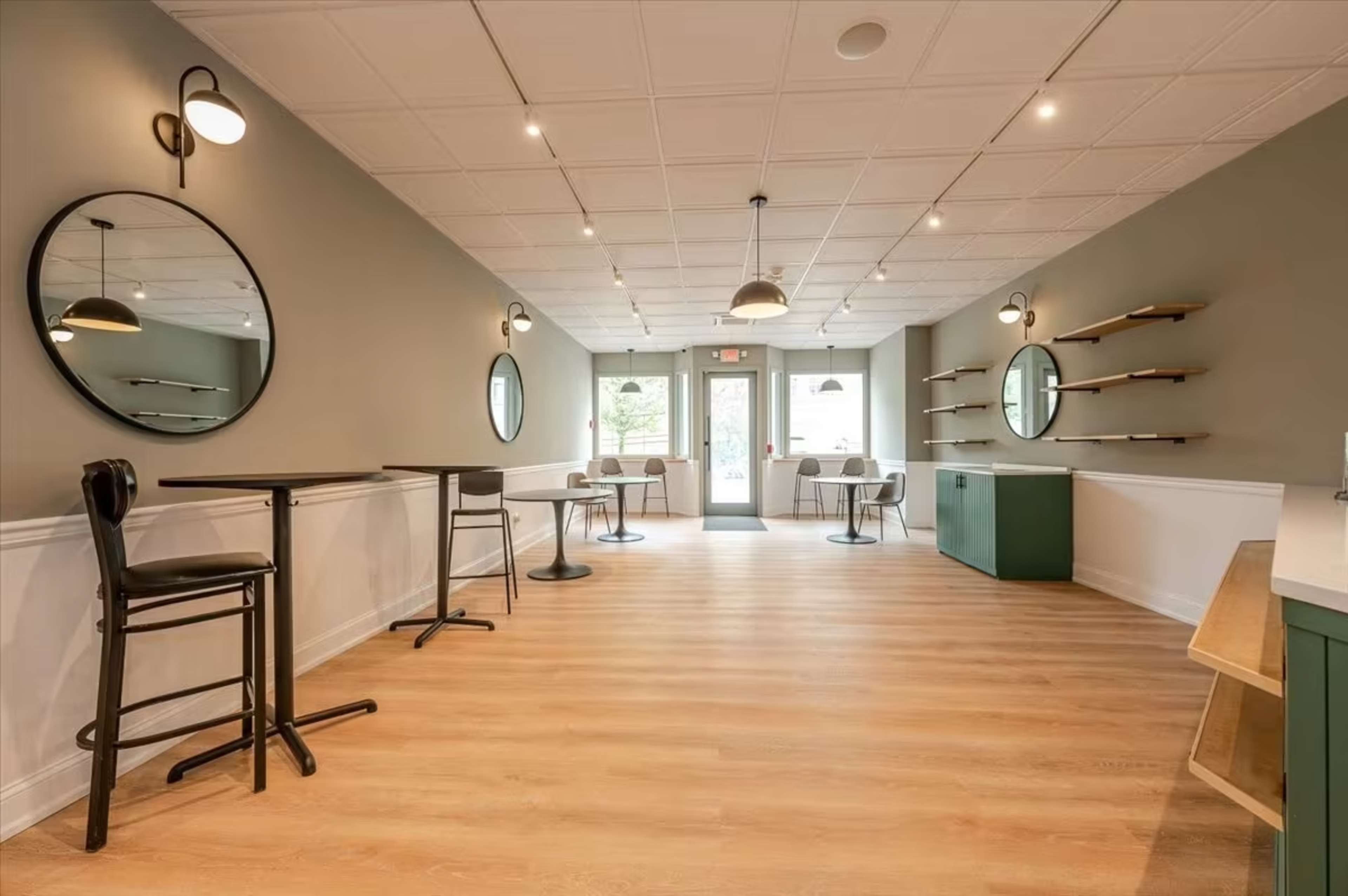 A modern interior of a café with a light wooden floor, circular mirrors on the walls, and a mix of high and low seating options.