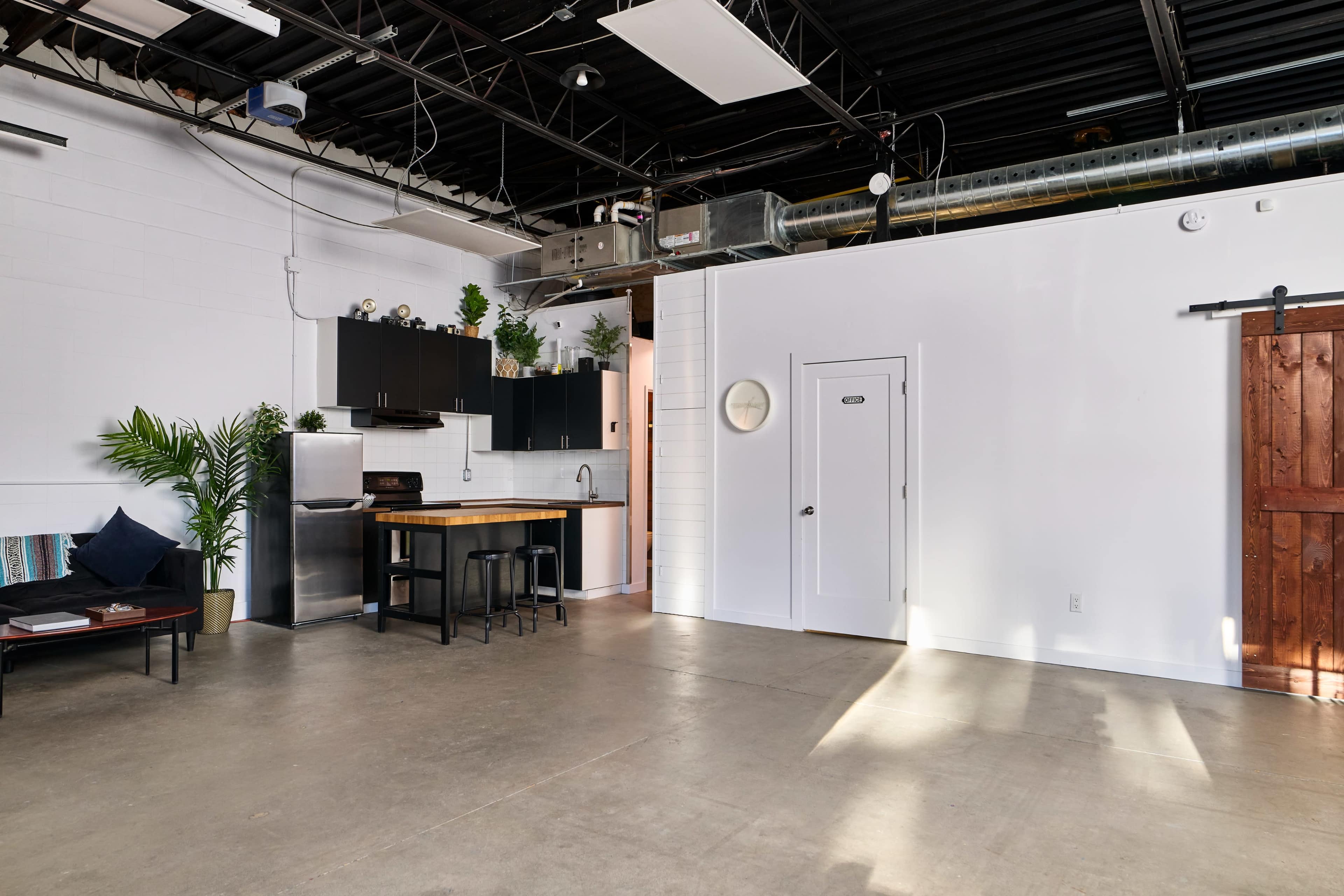 The image shows a spacious, modern interior featuring an open floor plan with a kitchen area, a wooden table with stools, and a sliding door.