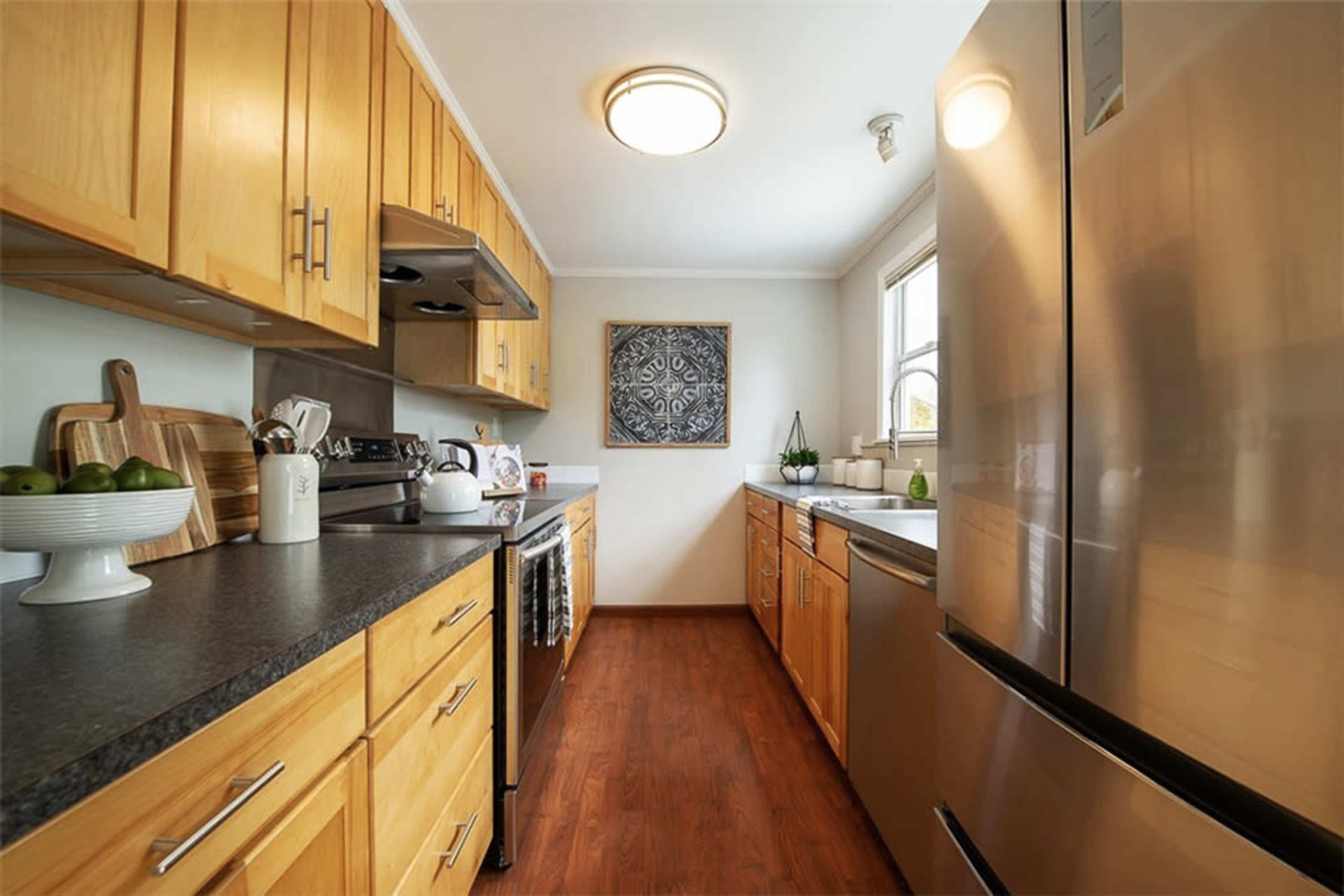 A modern kitchen with wooden cabinets, stainless steel appliances, and a countertop featuring a bowl of green apples.