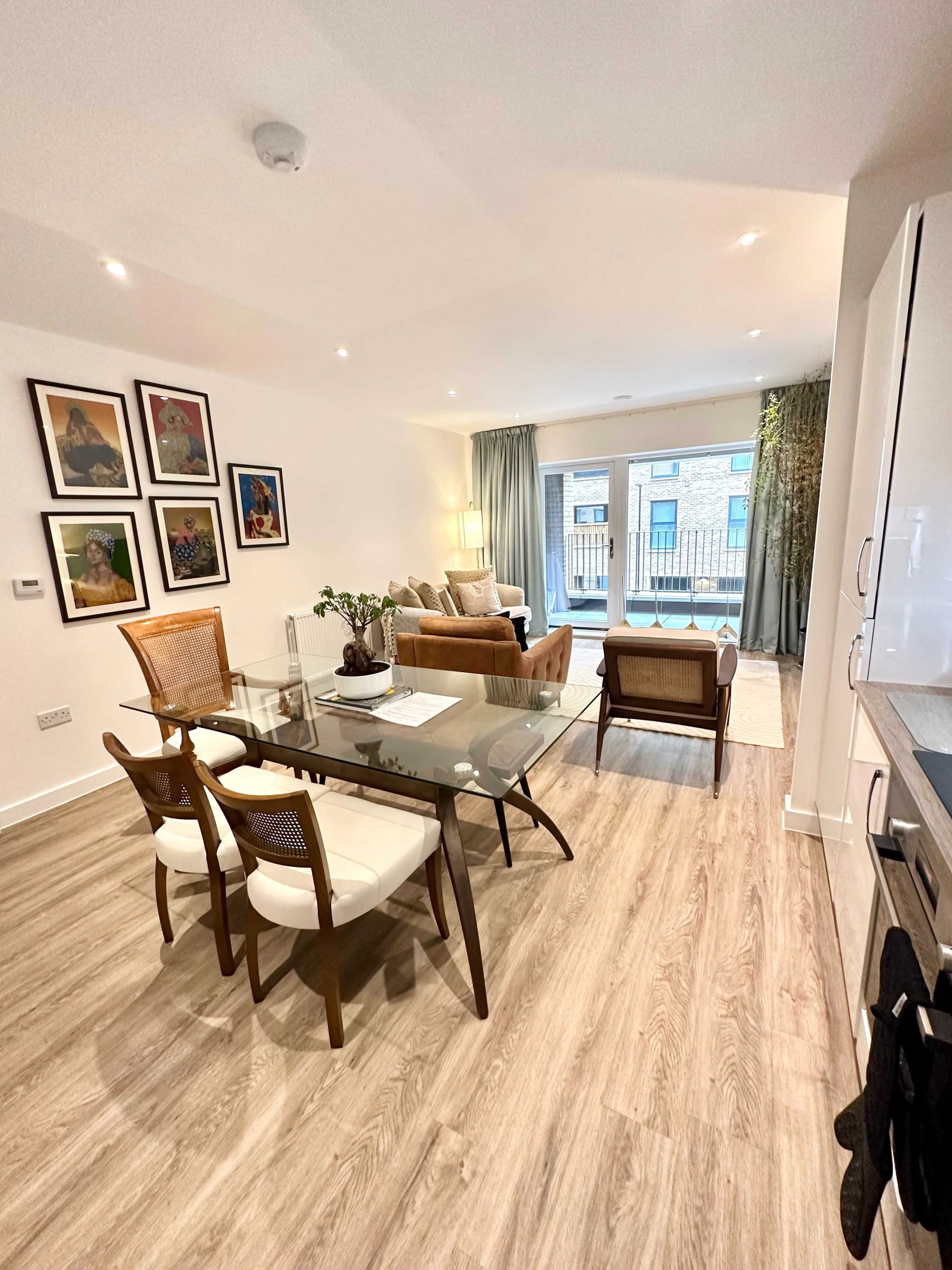 A modern living space features a dining area with a glass table and chairs, a seating area with a sofa, and large windows that open to a balcony.