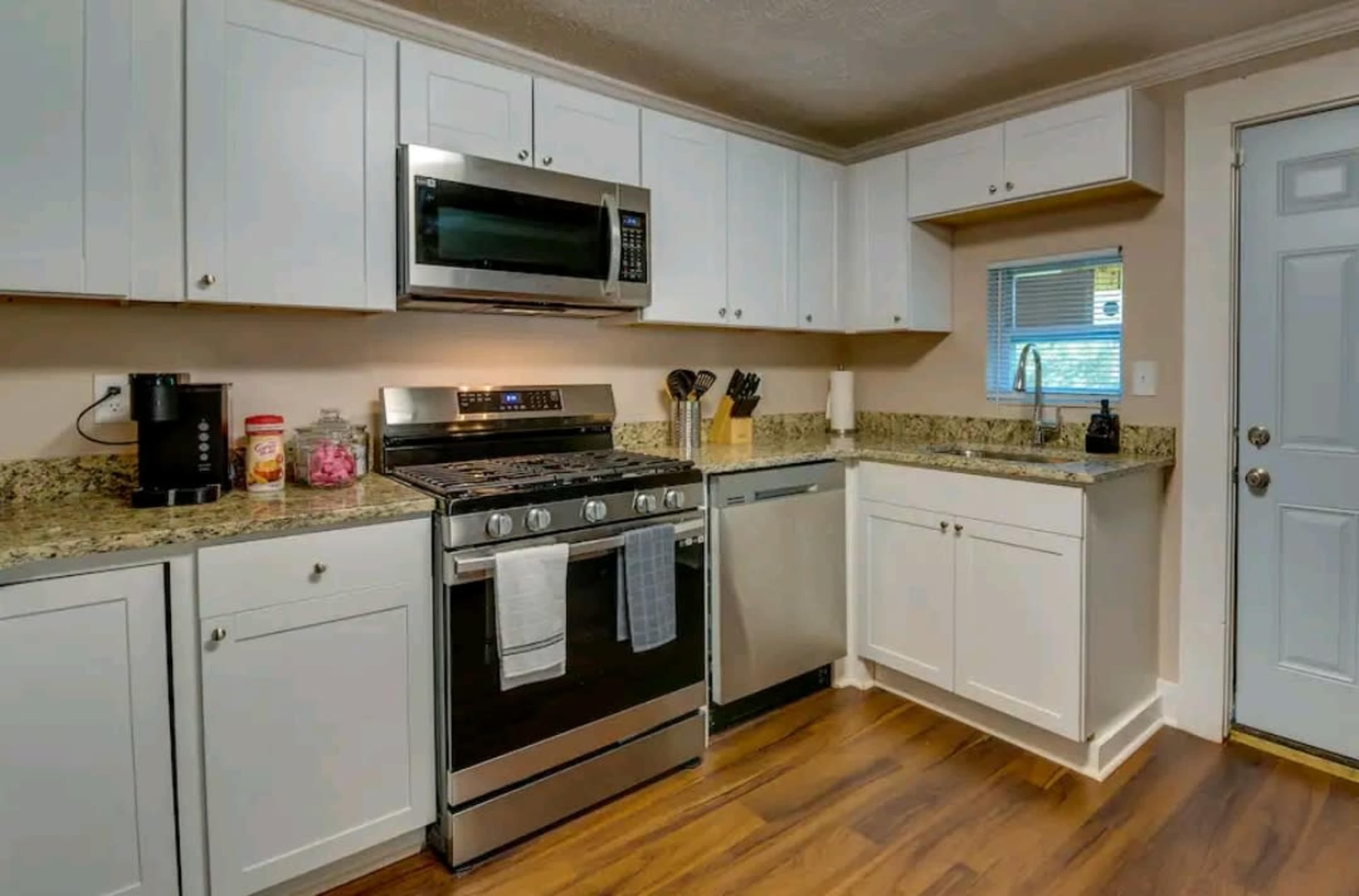 The image shows a modern kitchen with white cabinets, a stainless steel microwave, an oven, a dishwasher, and a door leading outside.