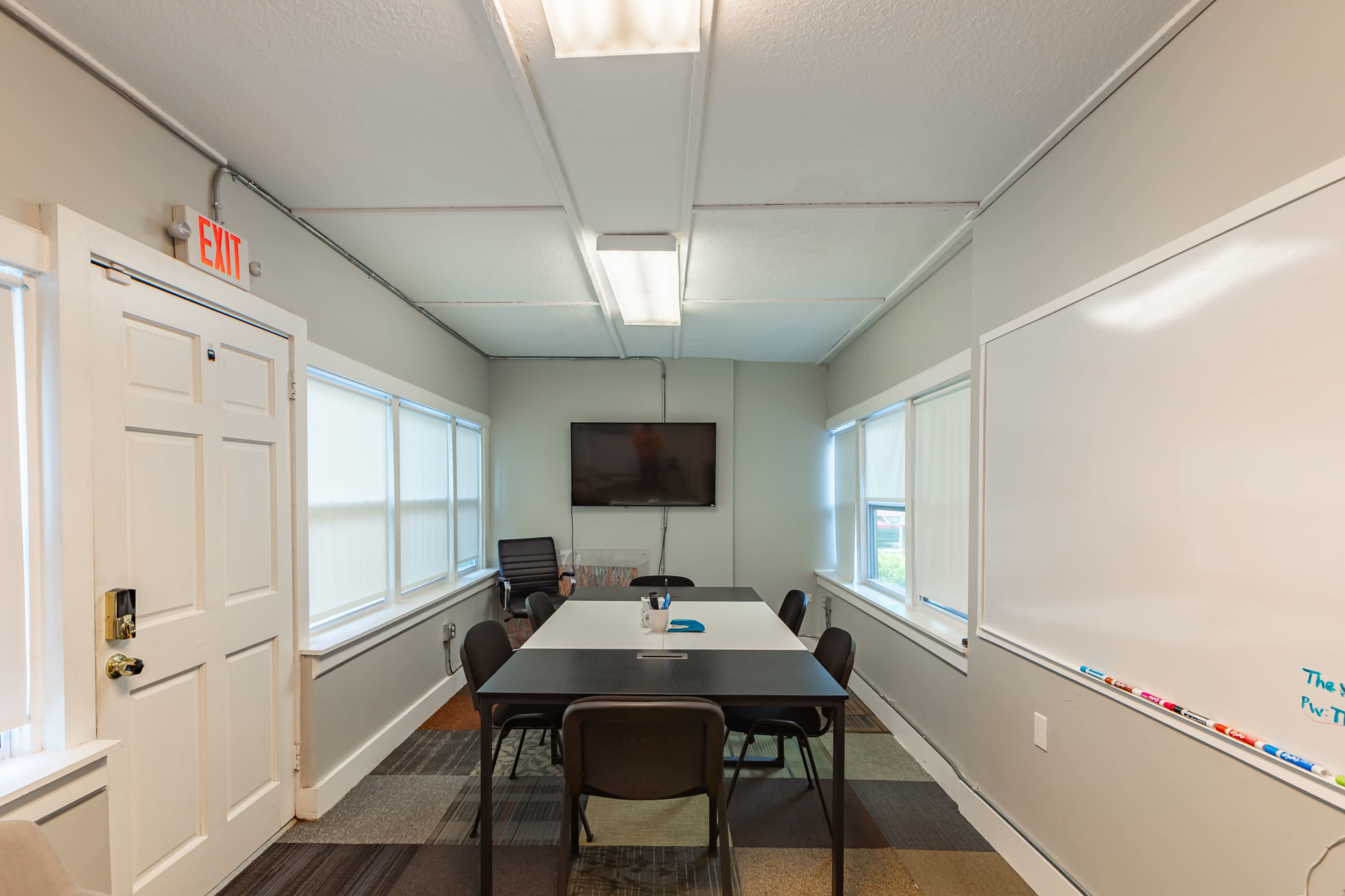 A conference room featuring a long table with chairs, a television mounted on the wall, and a whiteboard.