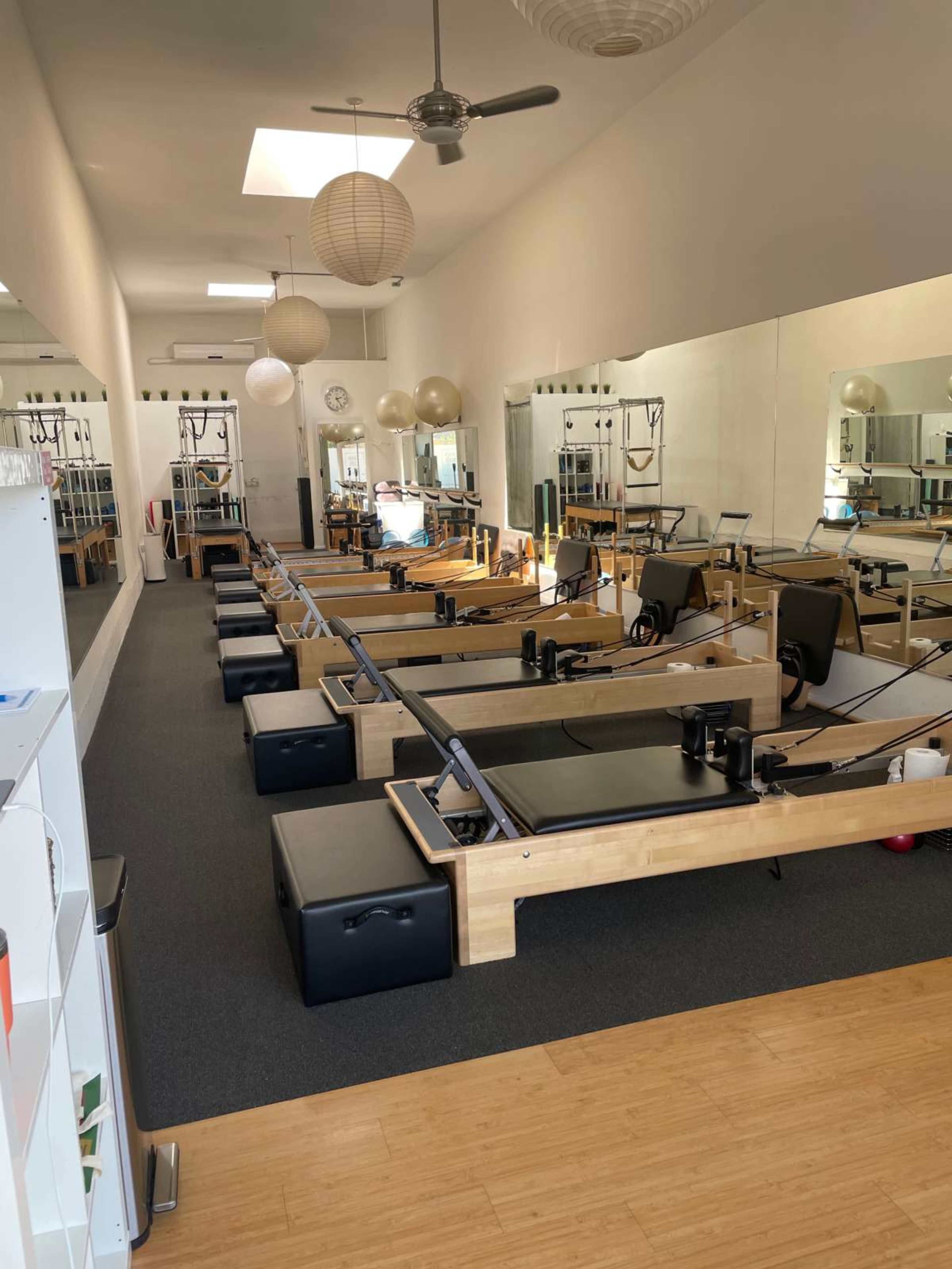 A Pilates studio features several reformer machines arranged in rows along a mirror-lined wall.