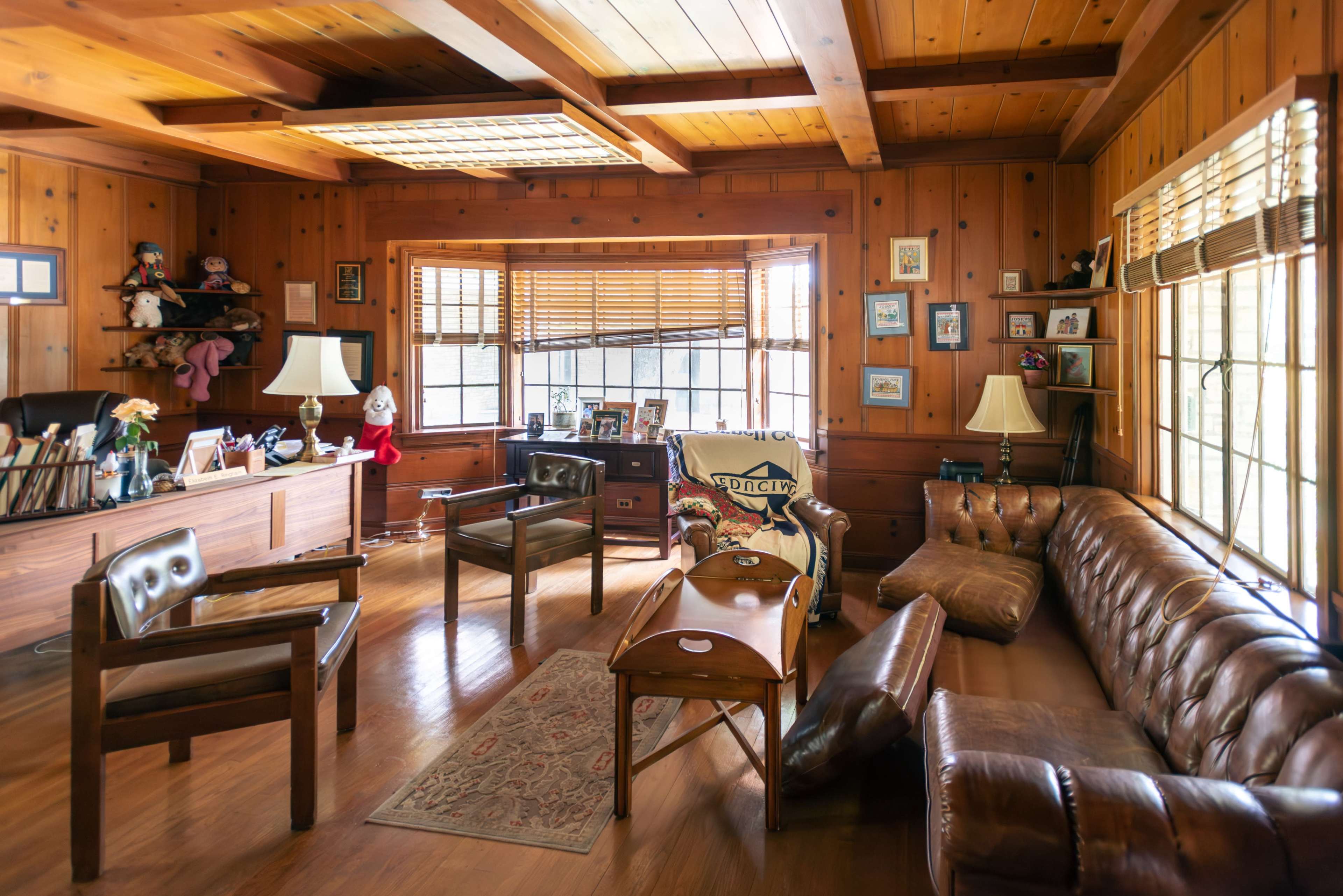 A wooden-paneled office with a seating area, a large desk, and numerous framed pictures on the walls.