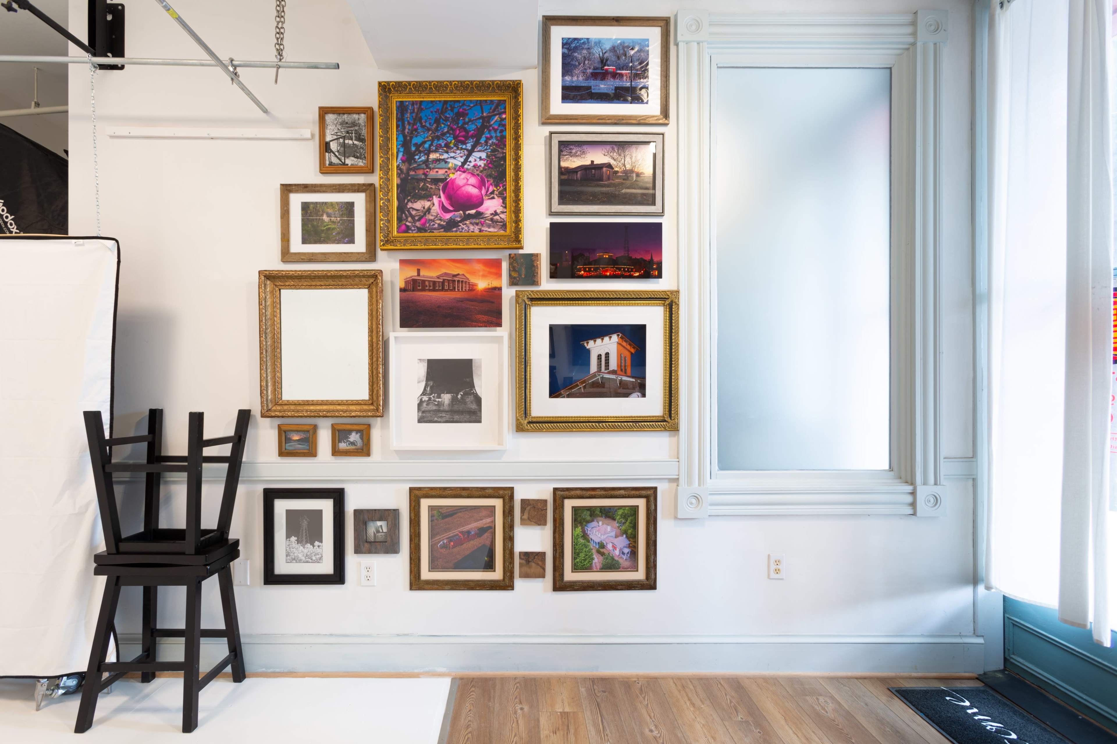 A wall adorned with a variety of framed photographs and artwork alongside a black chair in an interior space.