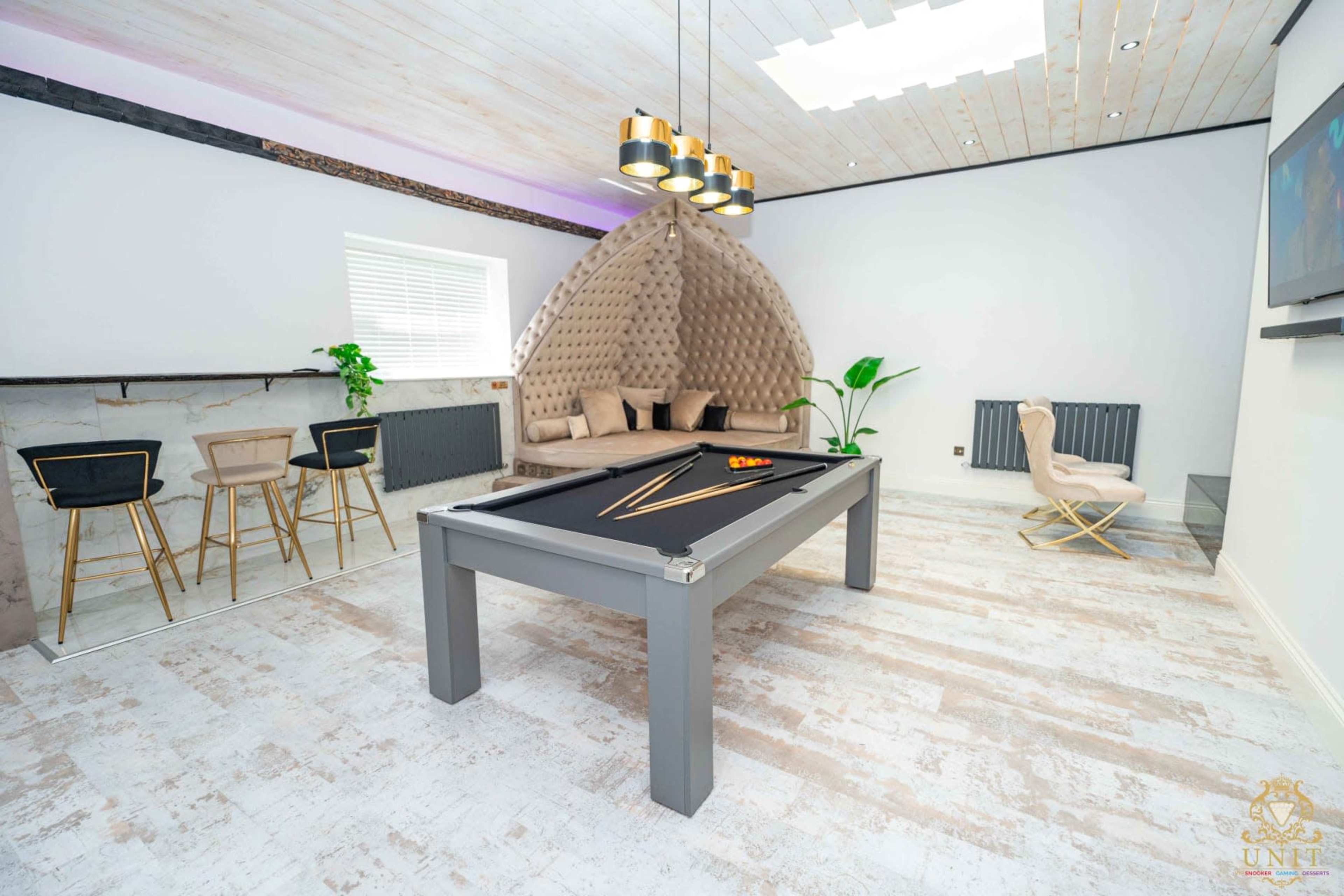 The image shows a modern game room featuring a billiard table, stylish seating, and a unique curved accent wall.