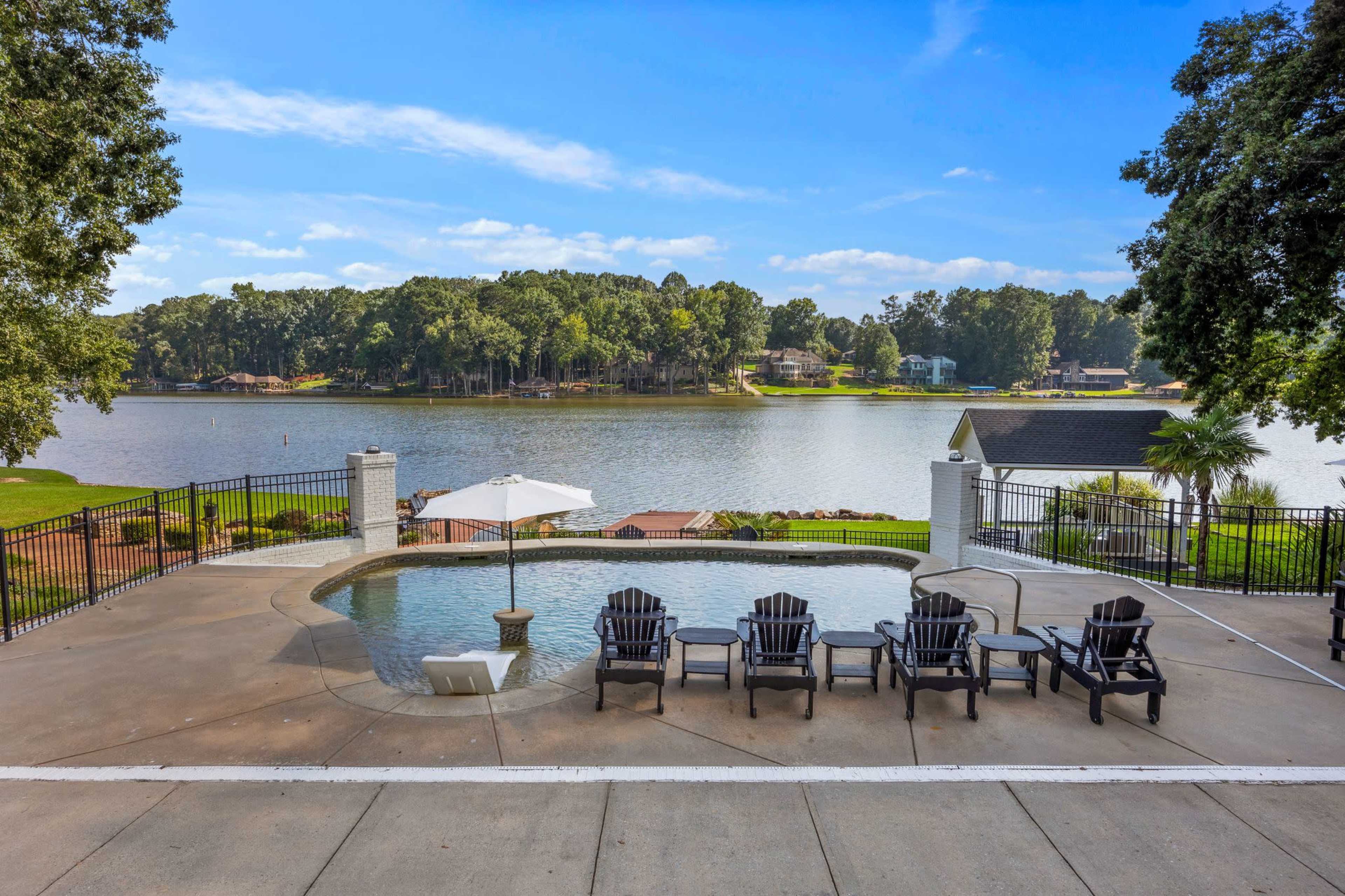 The image shows a poolside area with lounge chairs overlooking a lake surrounded by trees and houses.