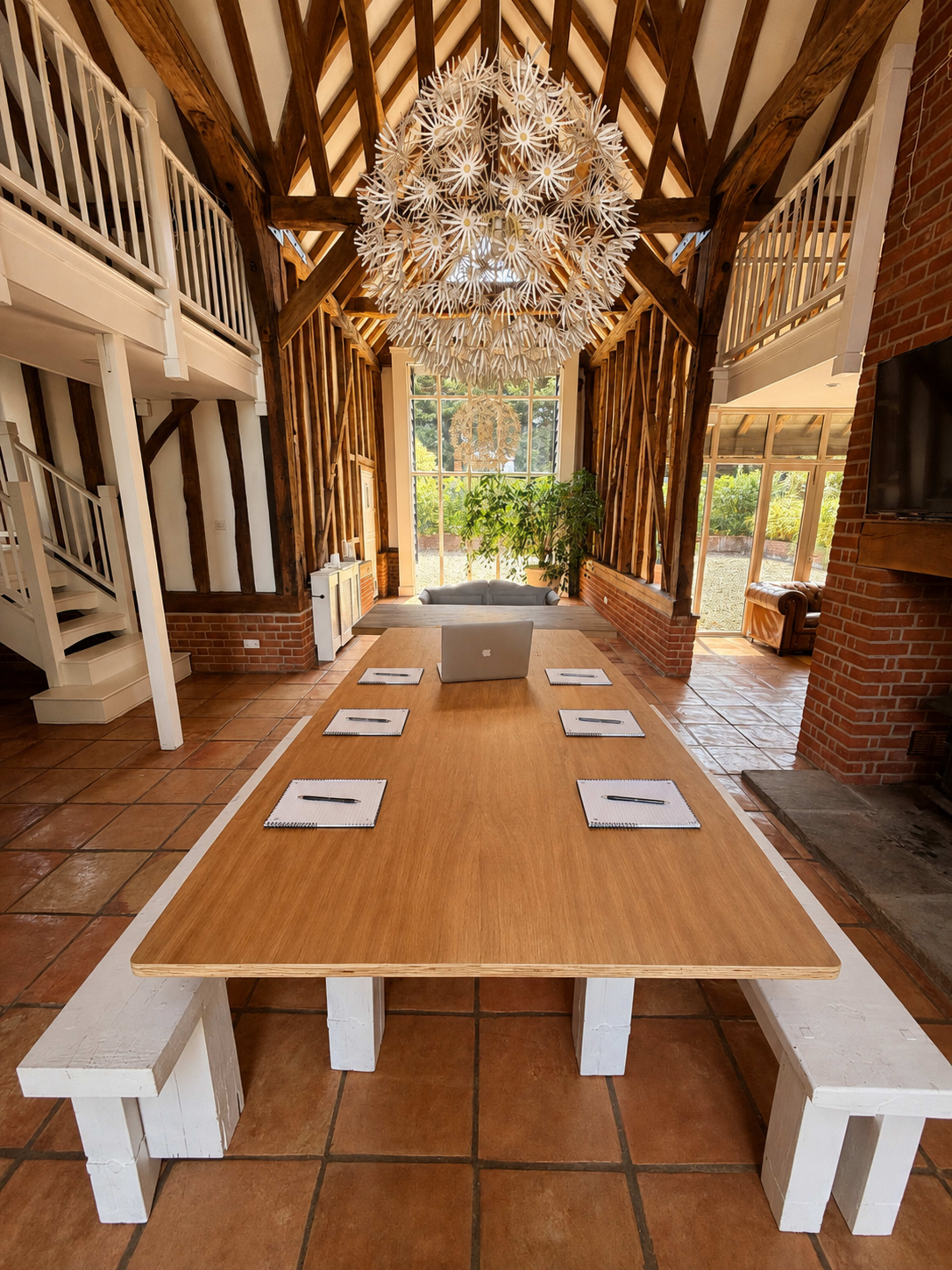 A large wooden table with several notepads is set up in a spacious room featuring exposed beams and a large decorative light fixture.