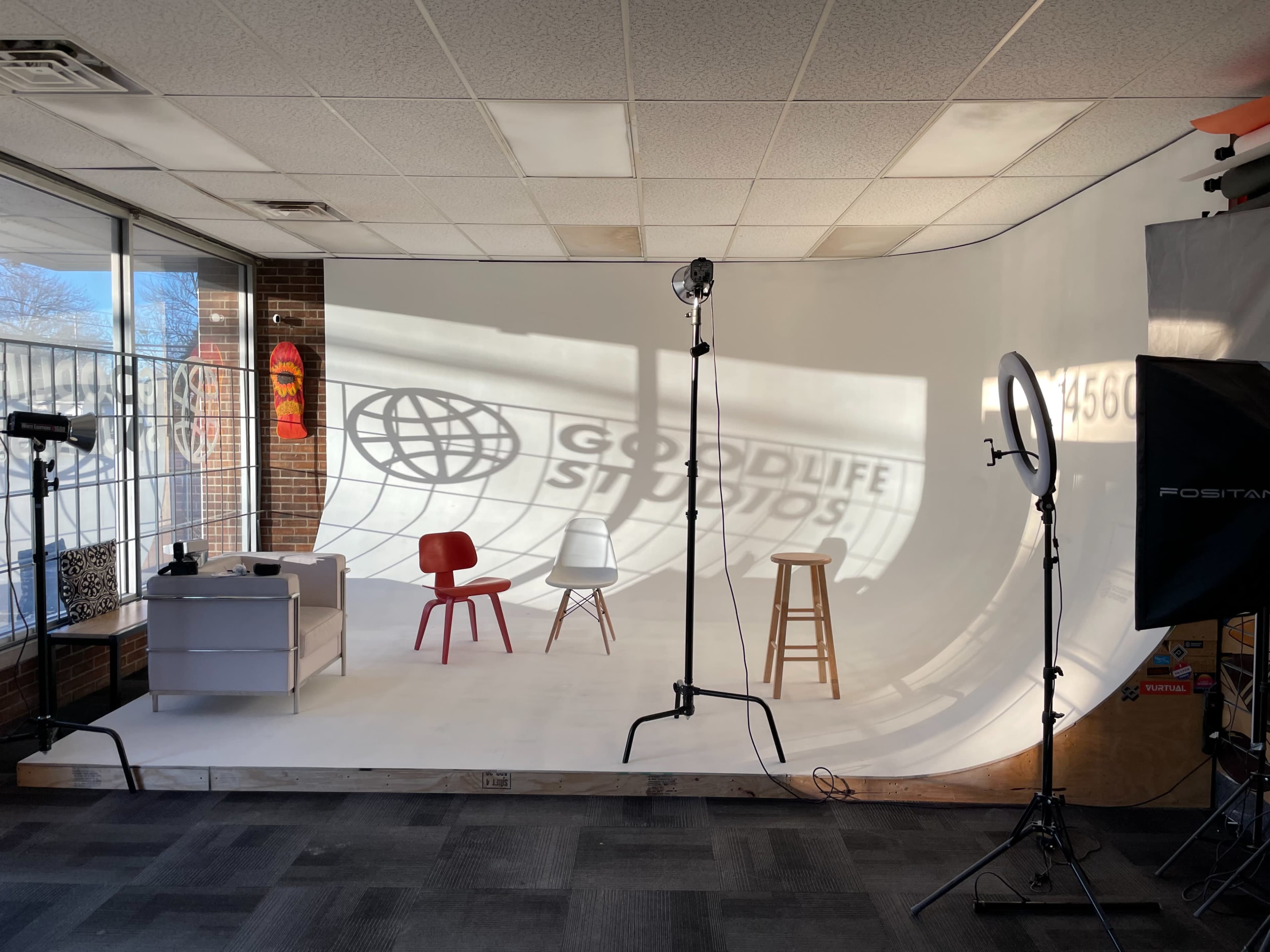 A photography studio set up with three chairs, a light stand, and a backdrop featuring the words "Goodlife Studios."