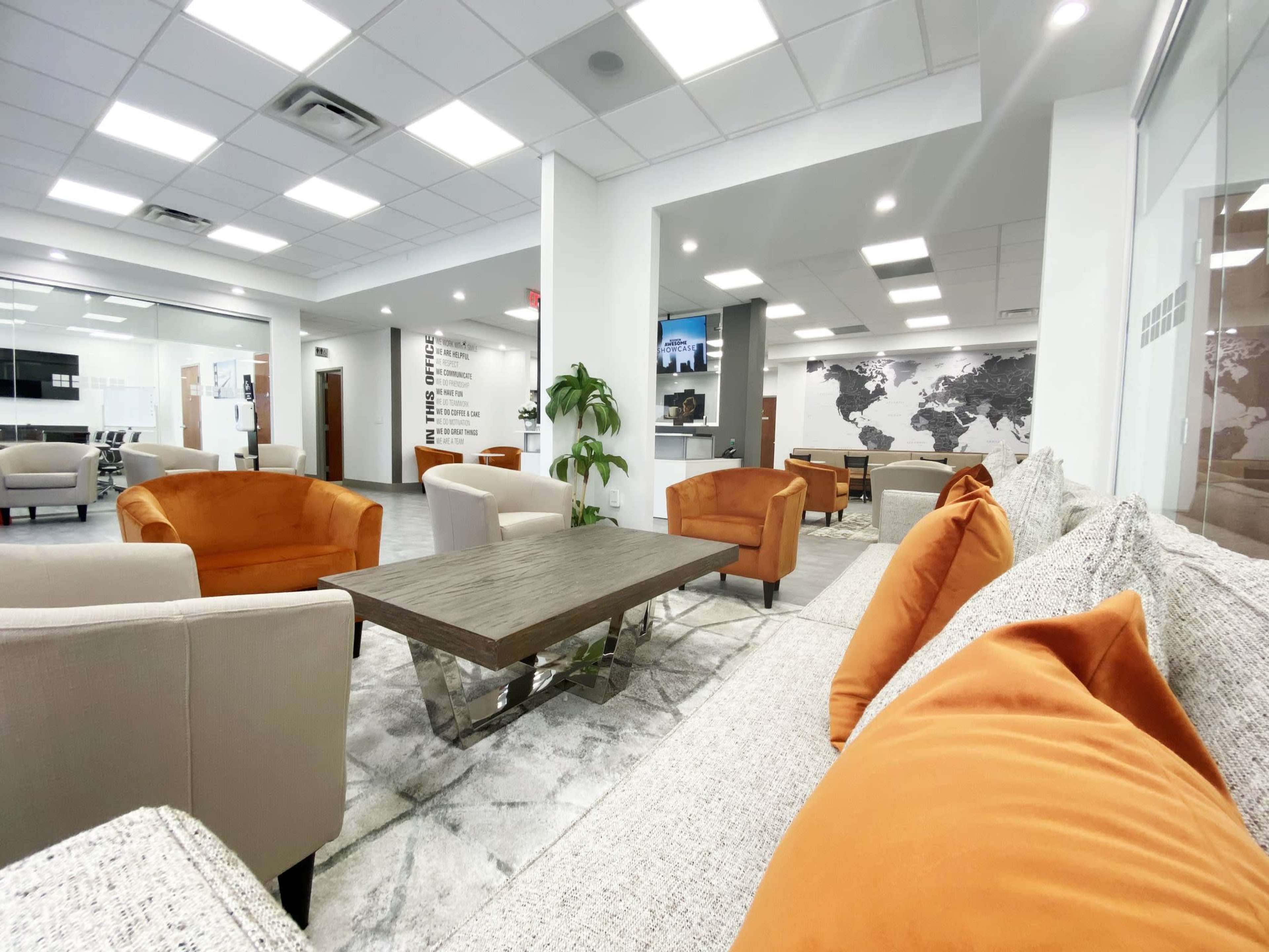 A modern office lounge area with orange armchairs and a large coffee table on a light rug, framed by a wall featuring a world map.