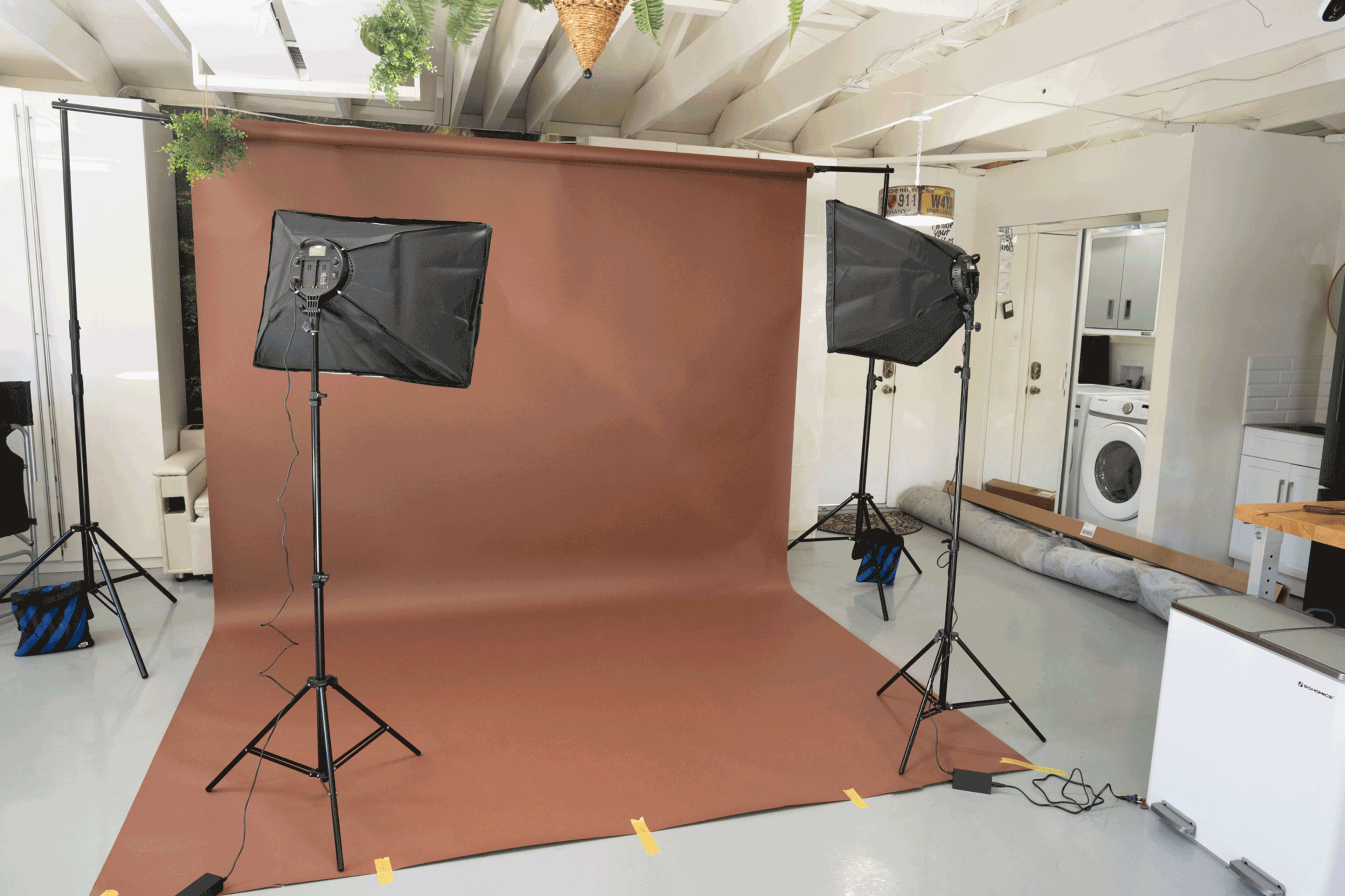 A photography studio setup with two softbox lights positioned on either side of a brown backdrop.