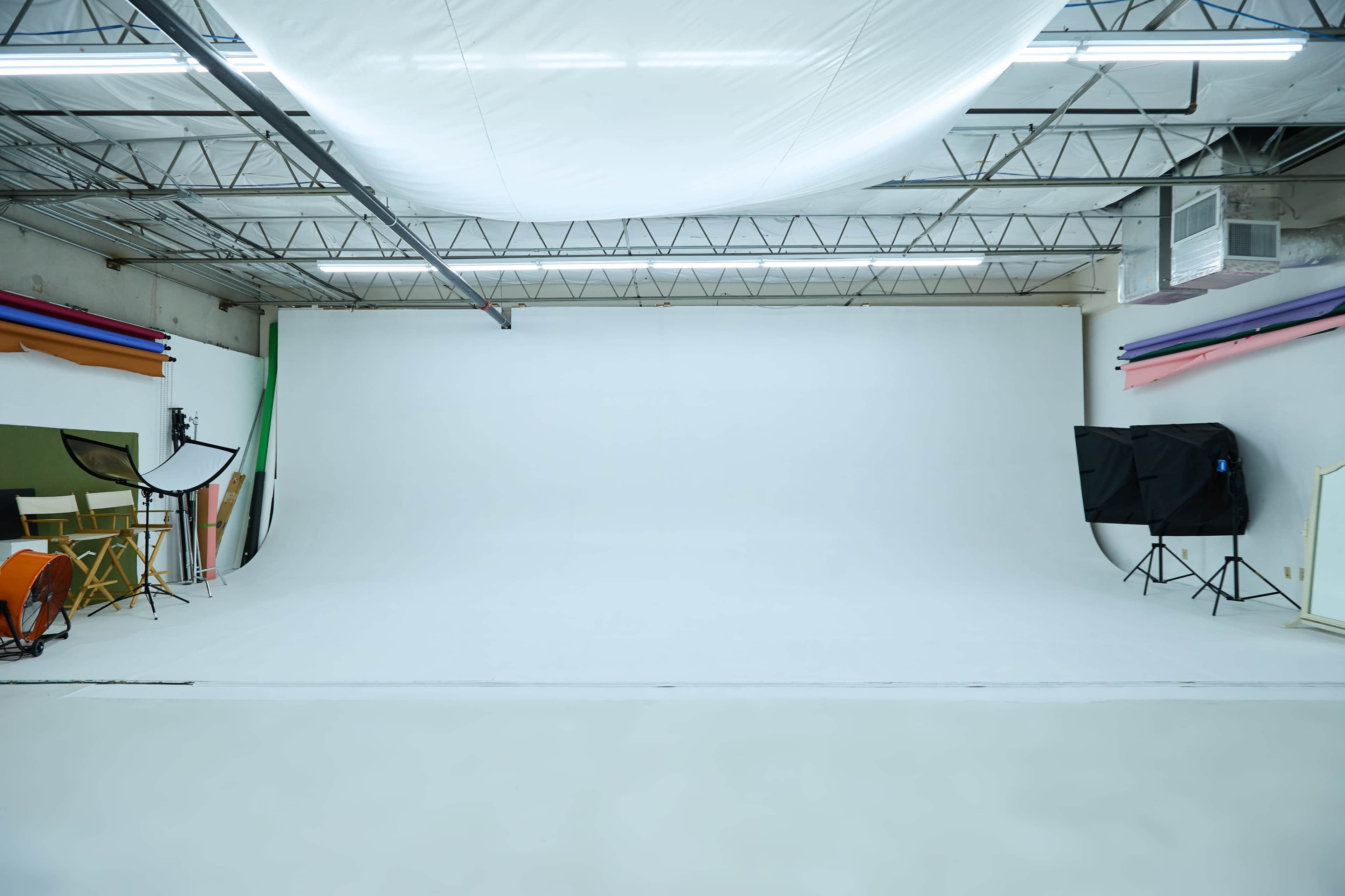 A spacious photography studio with a large white backdrop and various colorful backdrop rolls along the walls.