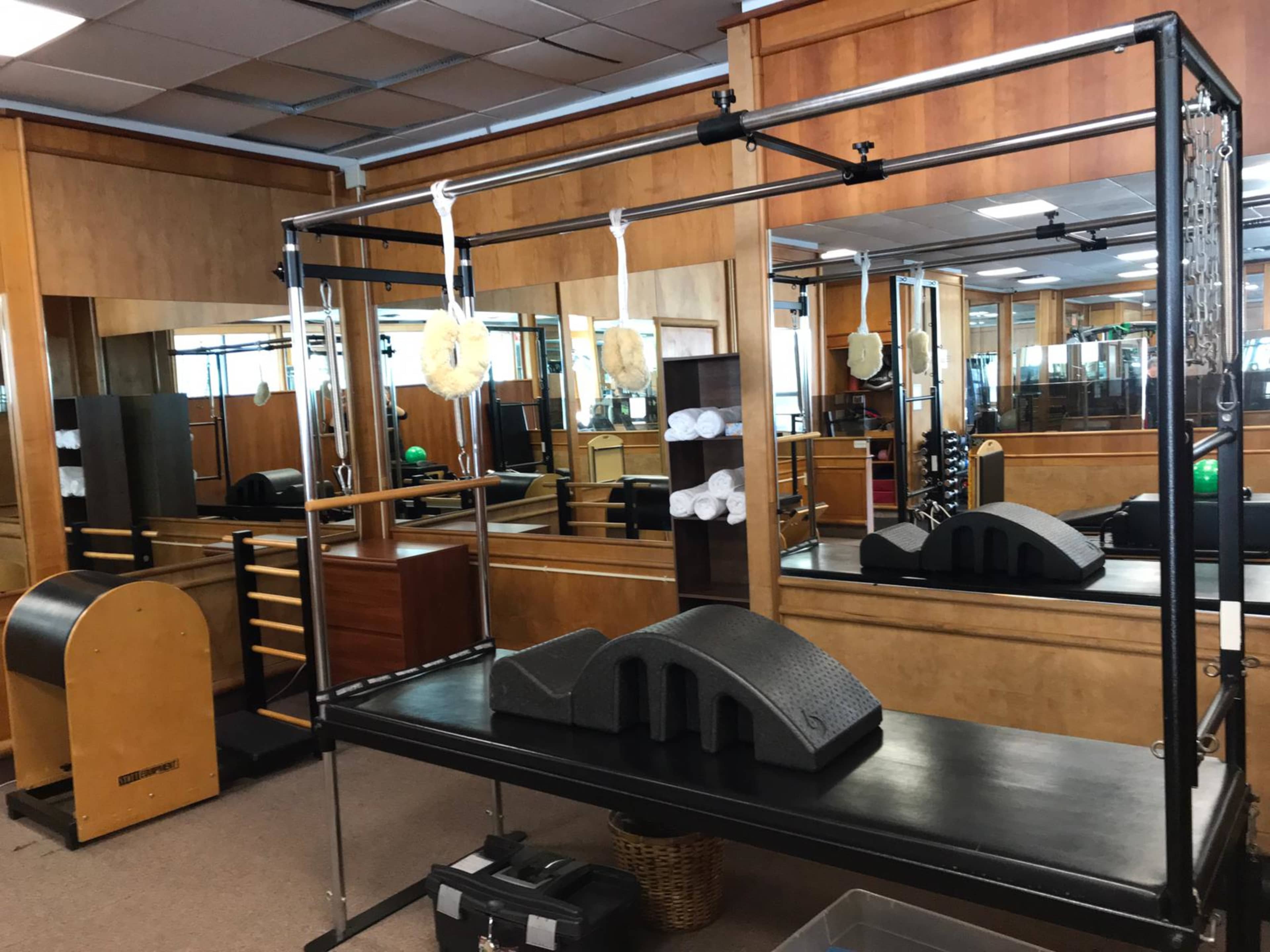 A fitness studio equipped with various exercise machines, a reformer, and mirrors along the walls.