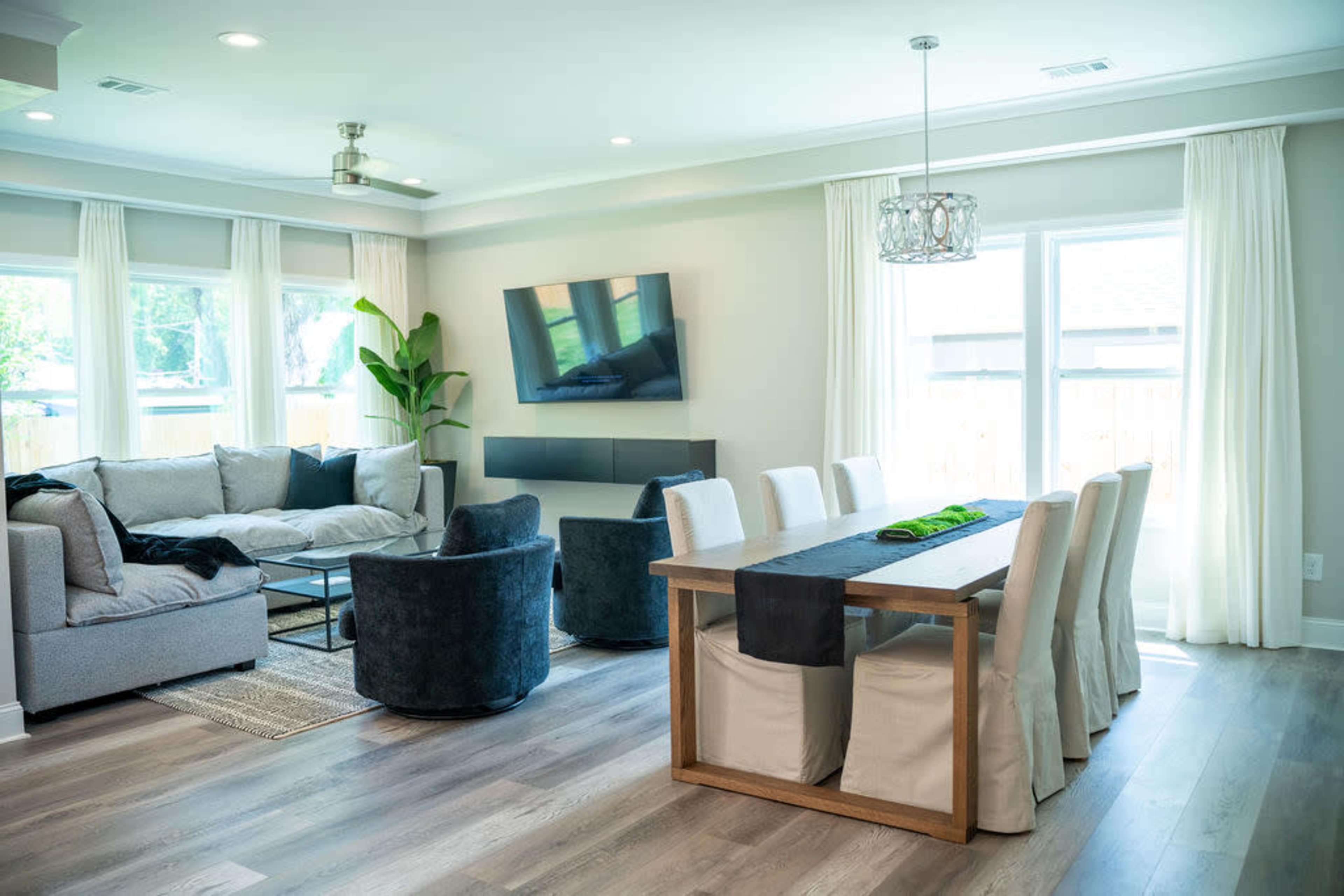 A modern living and dining area with a gray sectional sofa, dark chairs, and a wooden dining table set with white chairs.