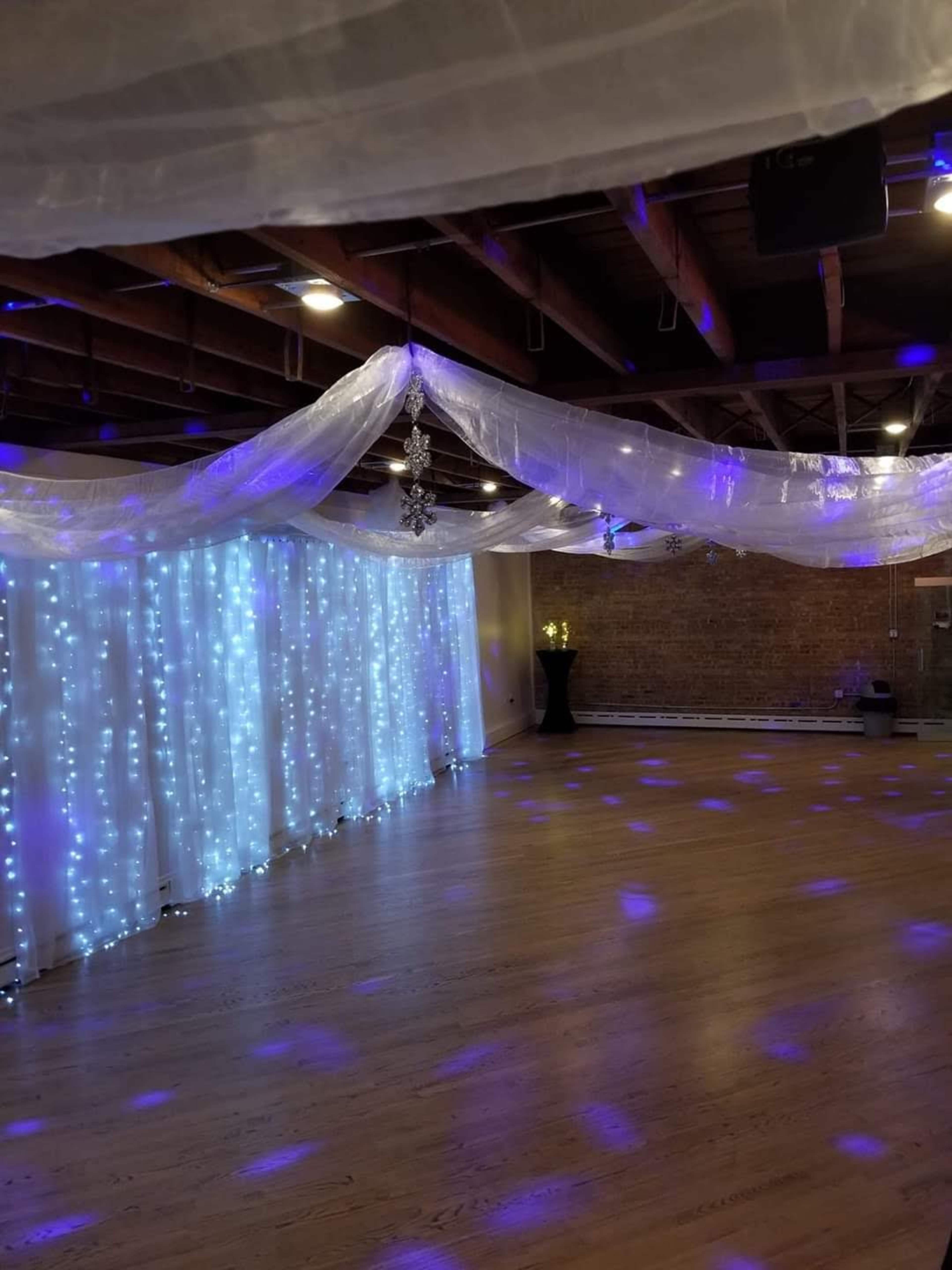 An indoor event space with draped white fabric and blue lights illuminating the walls and floor.
