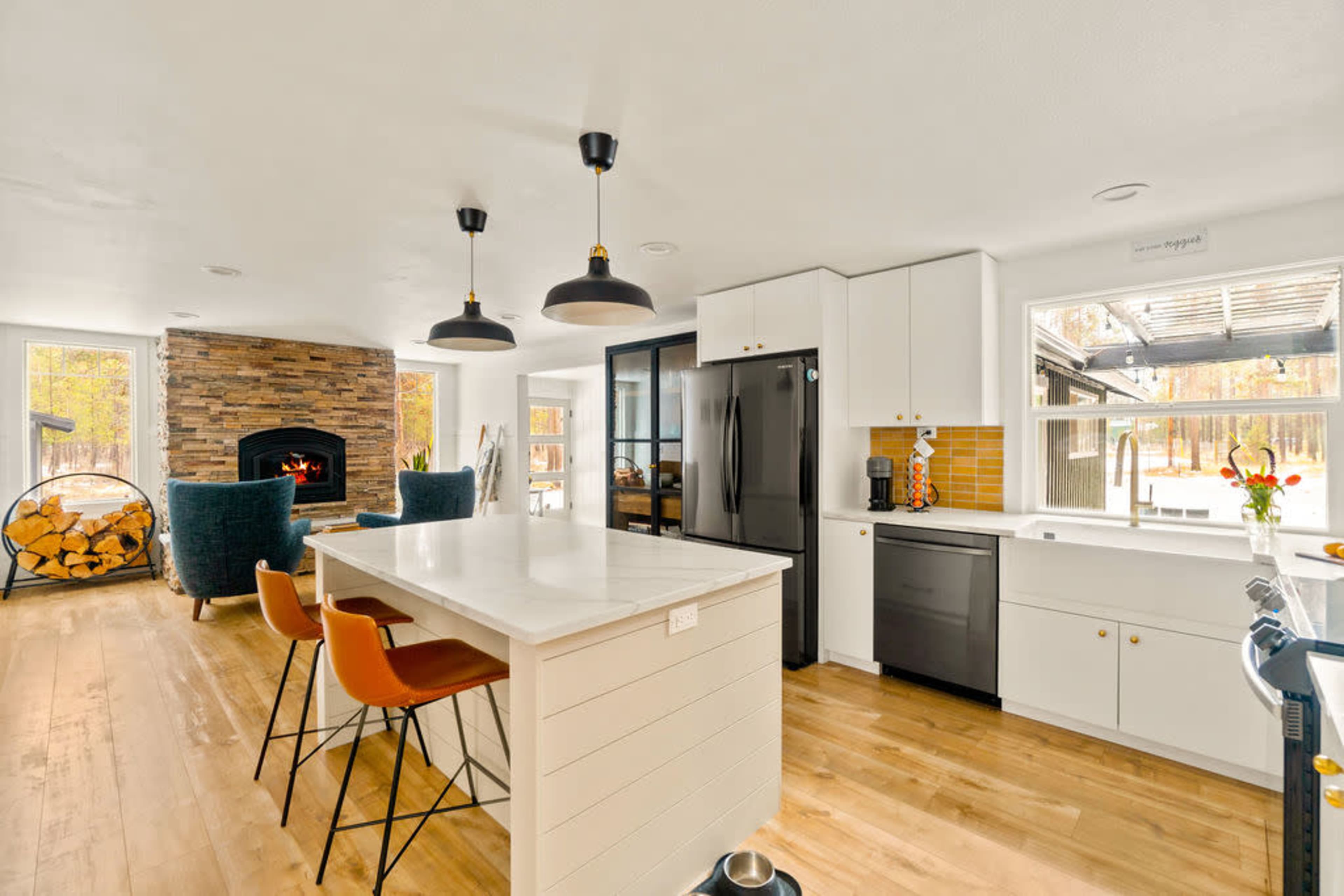 The kitchen features a central island with bar stools, modern appliances, and a stone fireplace in the background.
