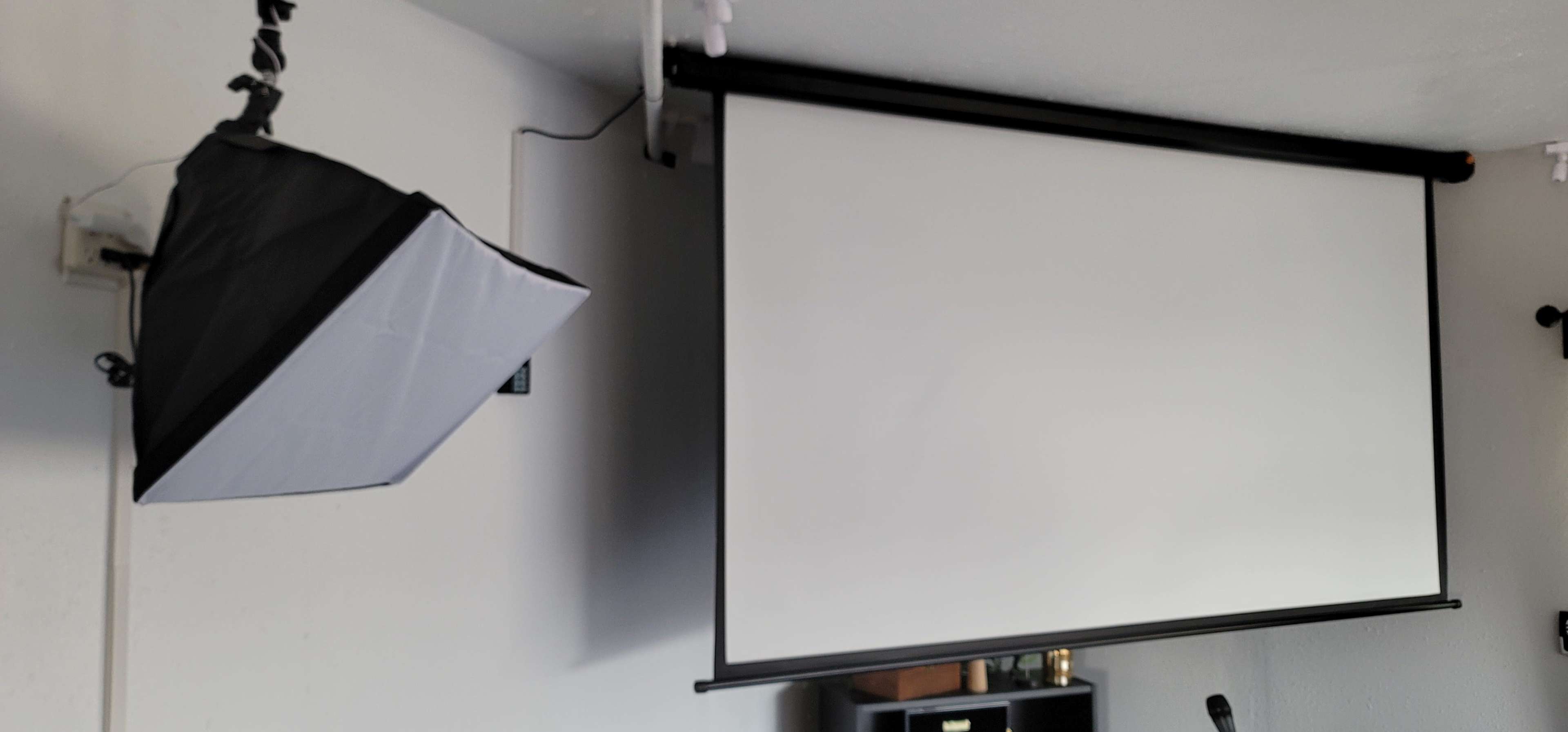 A black and white softbox is mounted on the wall next to a retractable white projection screen.
