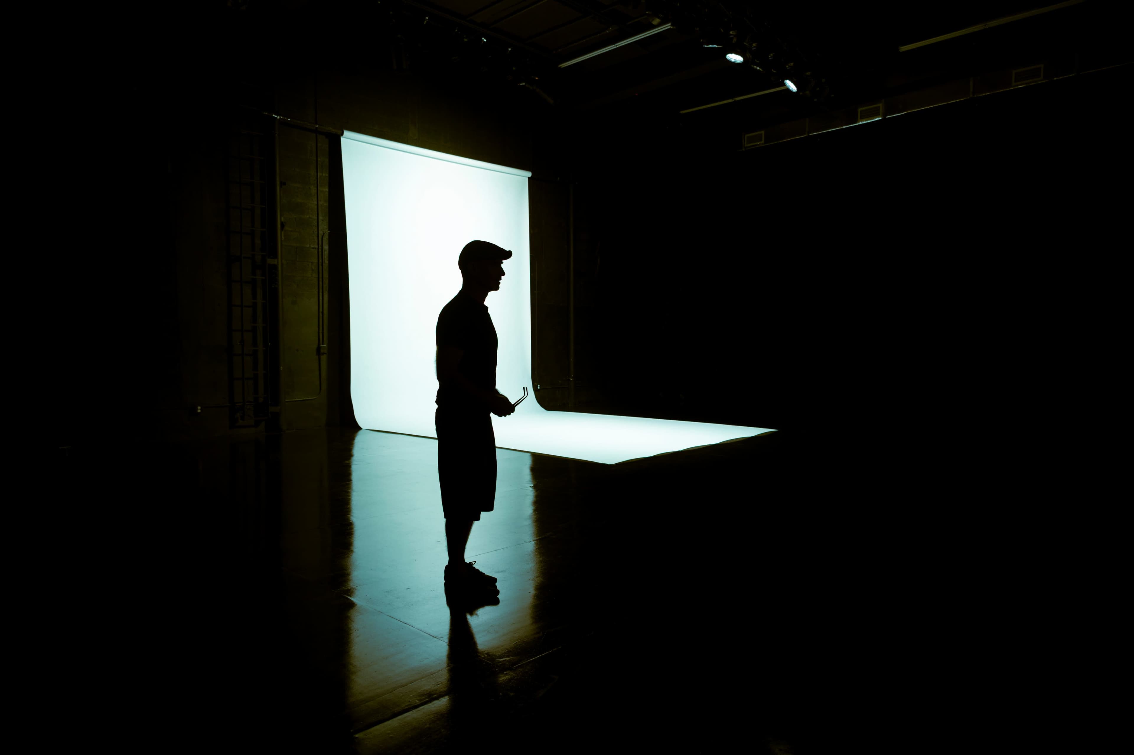 A silhouette of a person stands in a dimly lit studio in front of a softly illuminated backdrop.