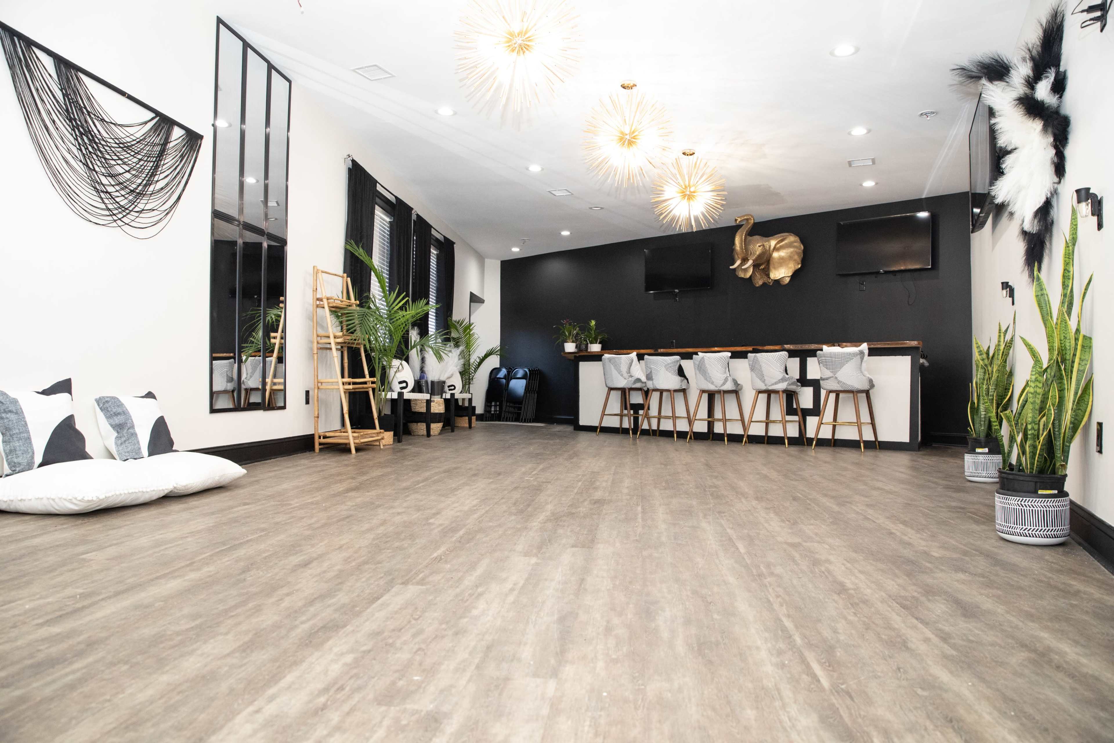A spacious room with modern decor, featuring a seating area with bar stools, plants, and decorative wall elements.