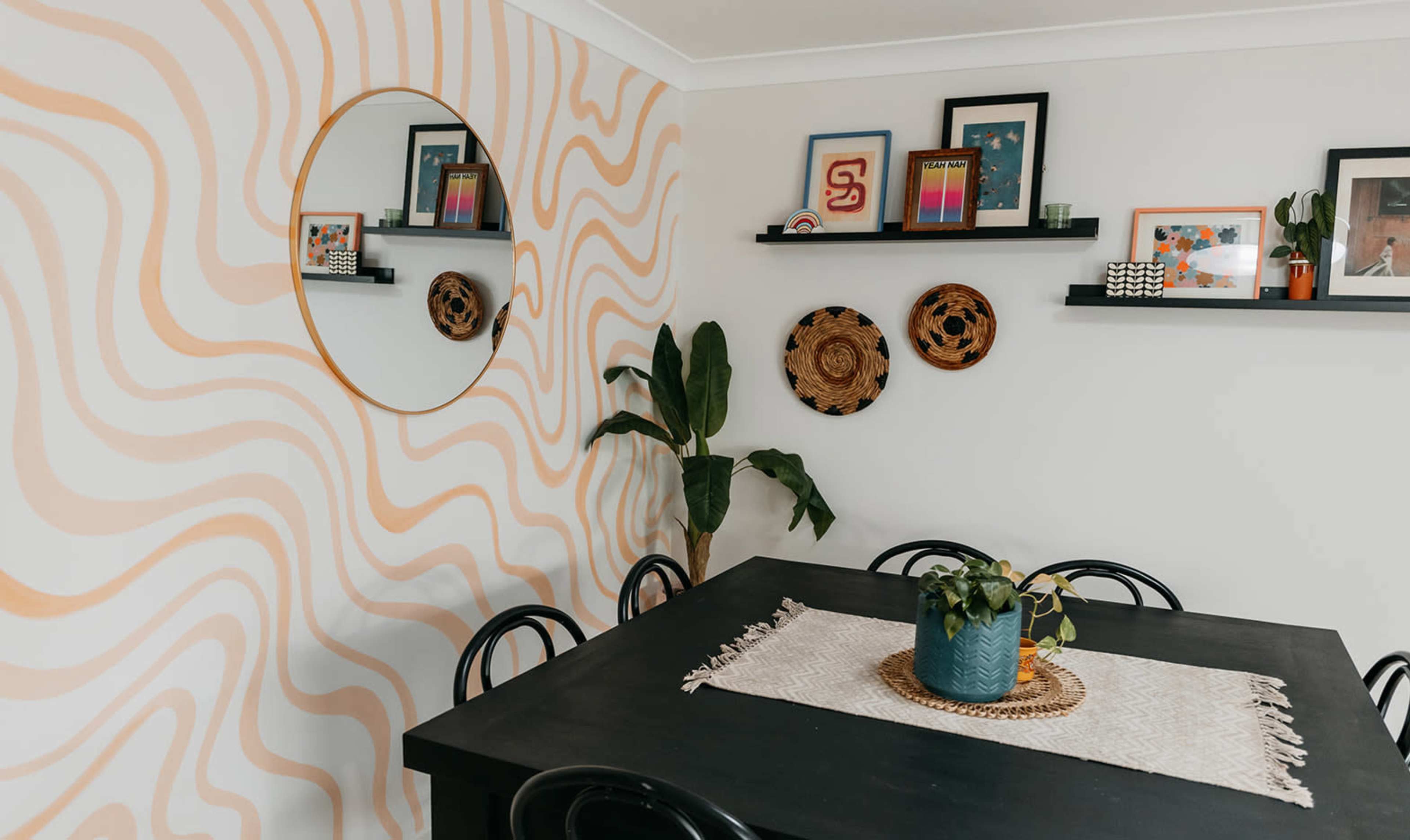 A dining area featuring a black table with a plant centerpiece, surrounded by chairs, and decorated with wall art and shelves displaying photos and woven decor.