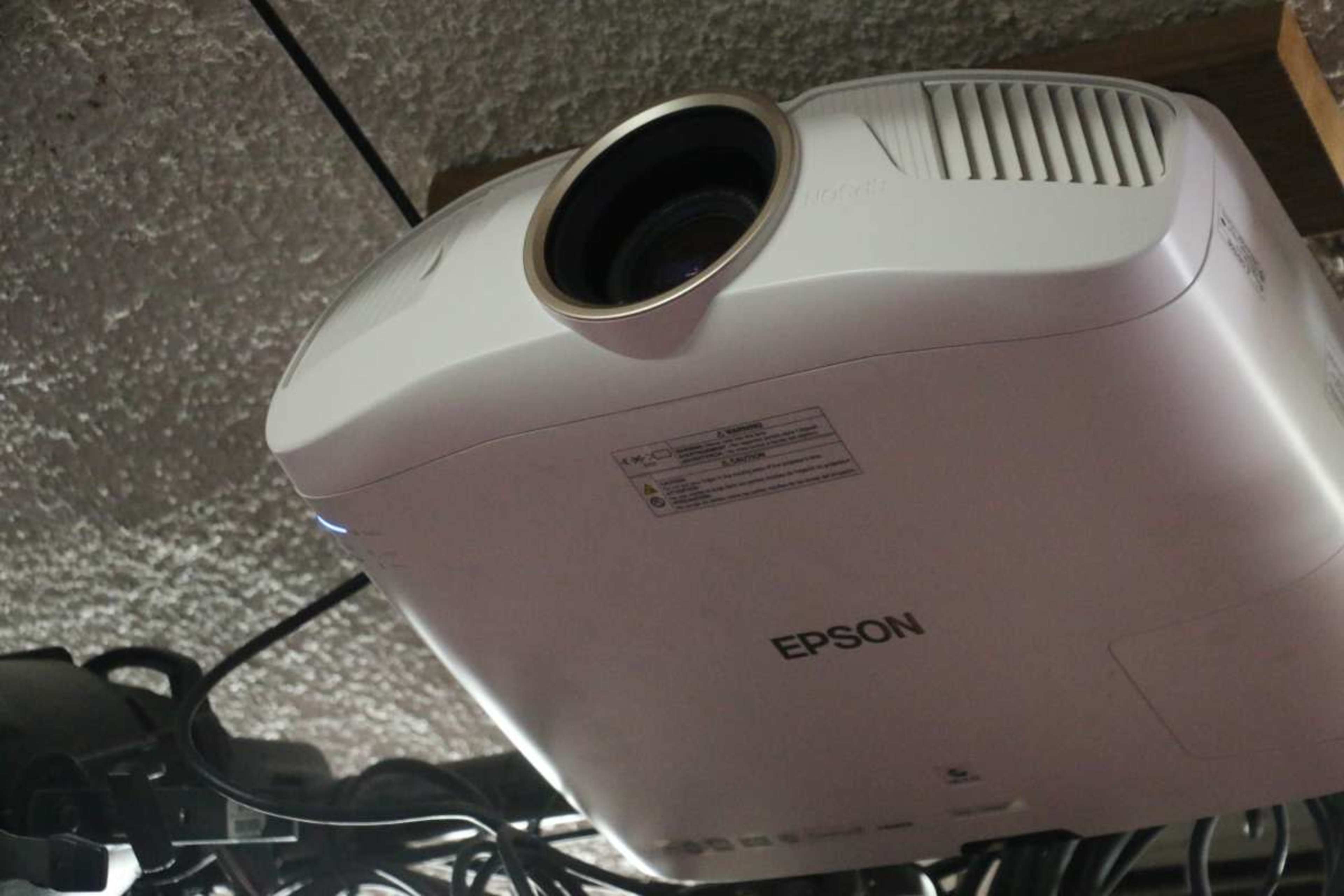 The image shows a white Epson projector mounted on a ceiling with visible cables attached.