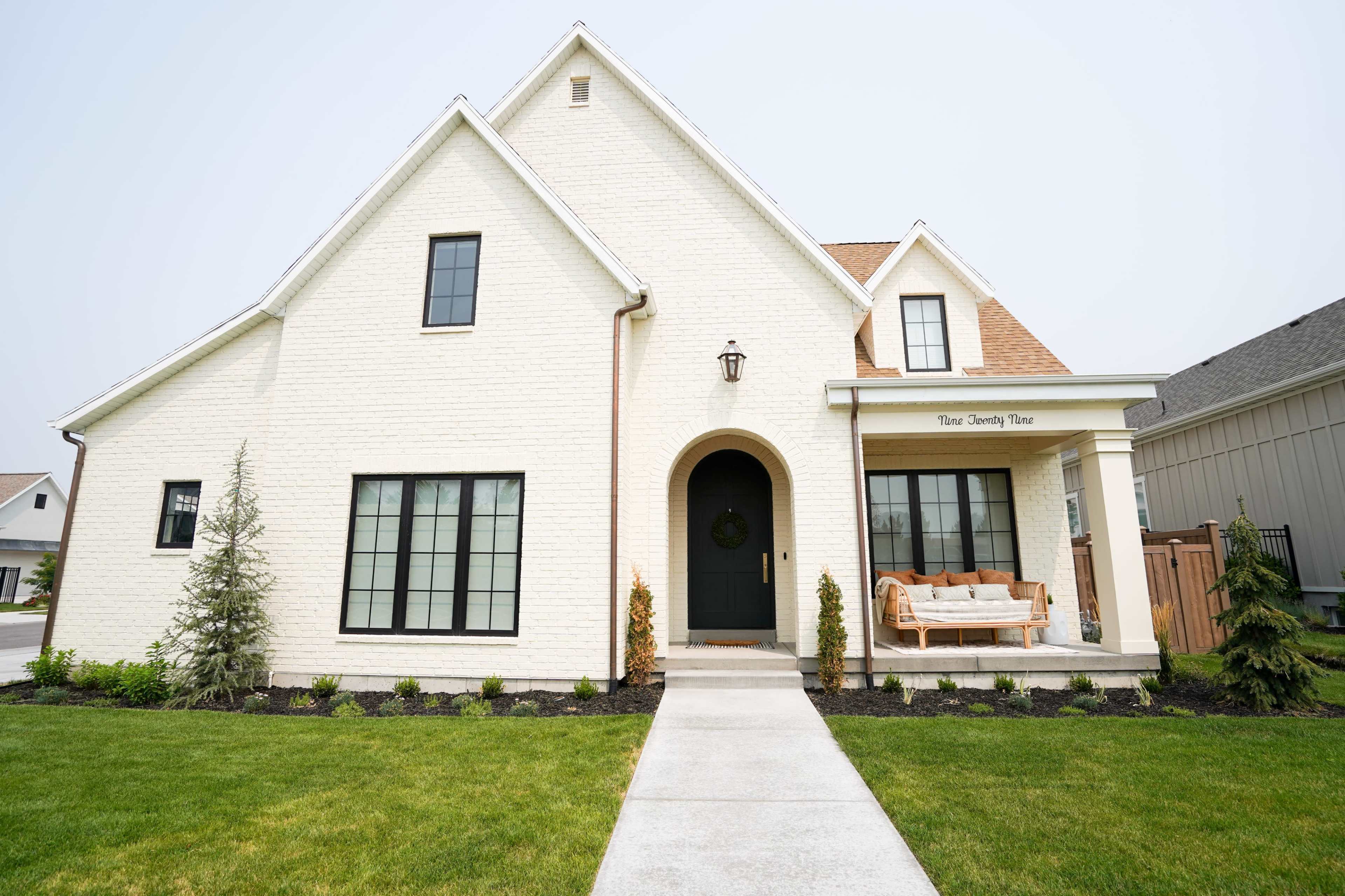 A modern white house with a dark front door and large windows is surrounded by manicured lawns and landscaping.