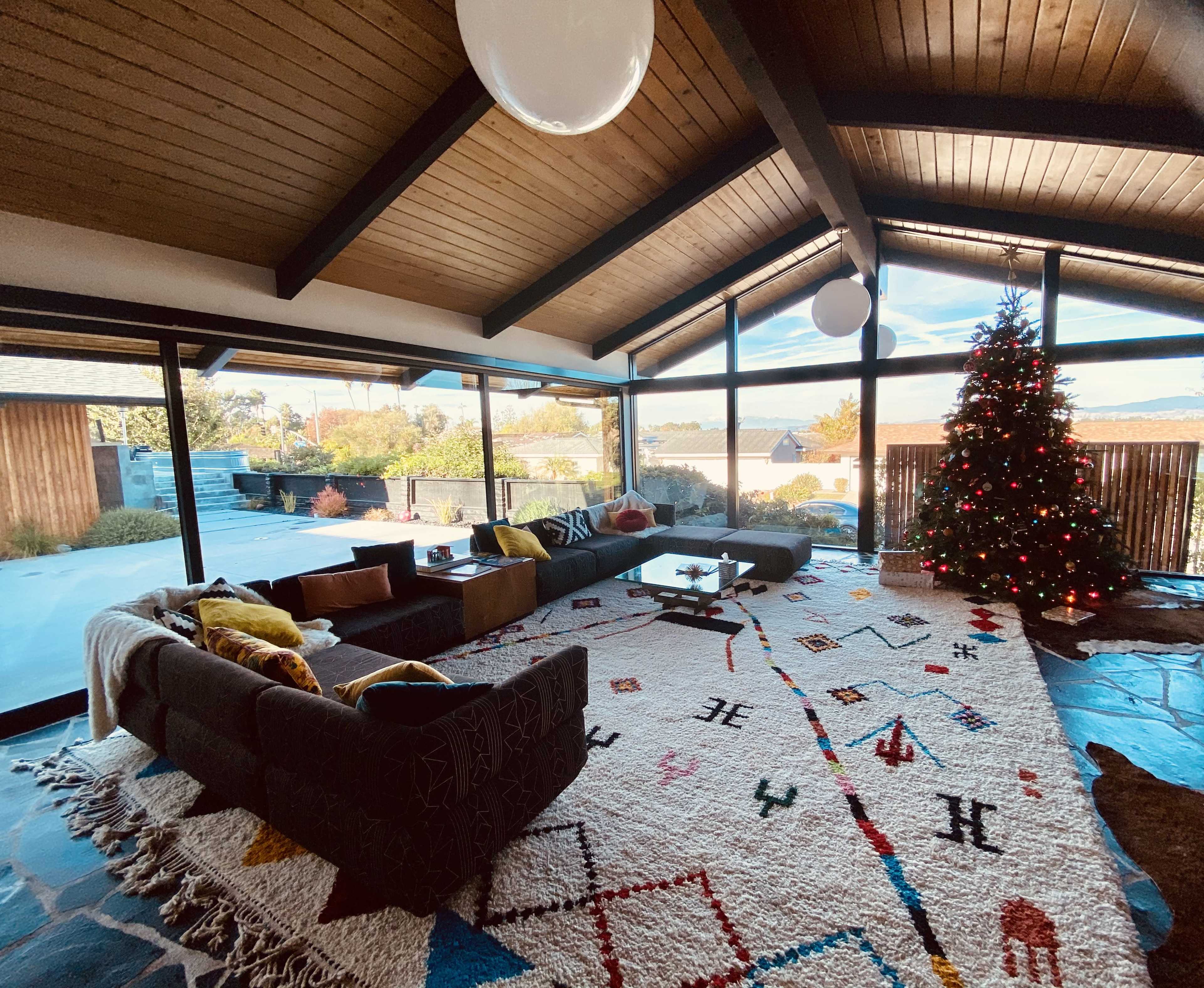 A spacious living room features a large area rug, modern furnishings, and a Christmas tree adorned with lights.