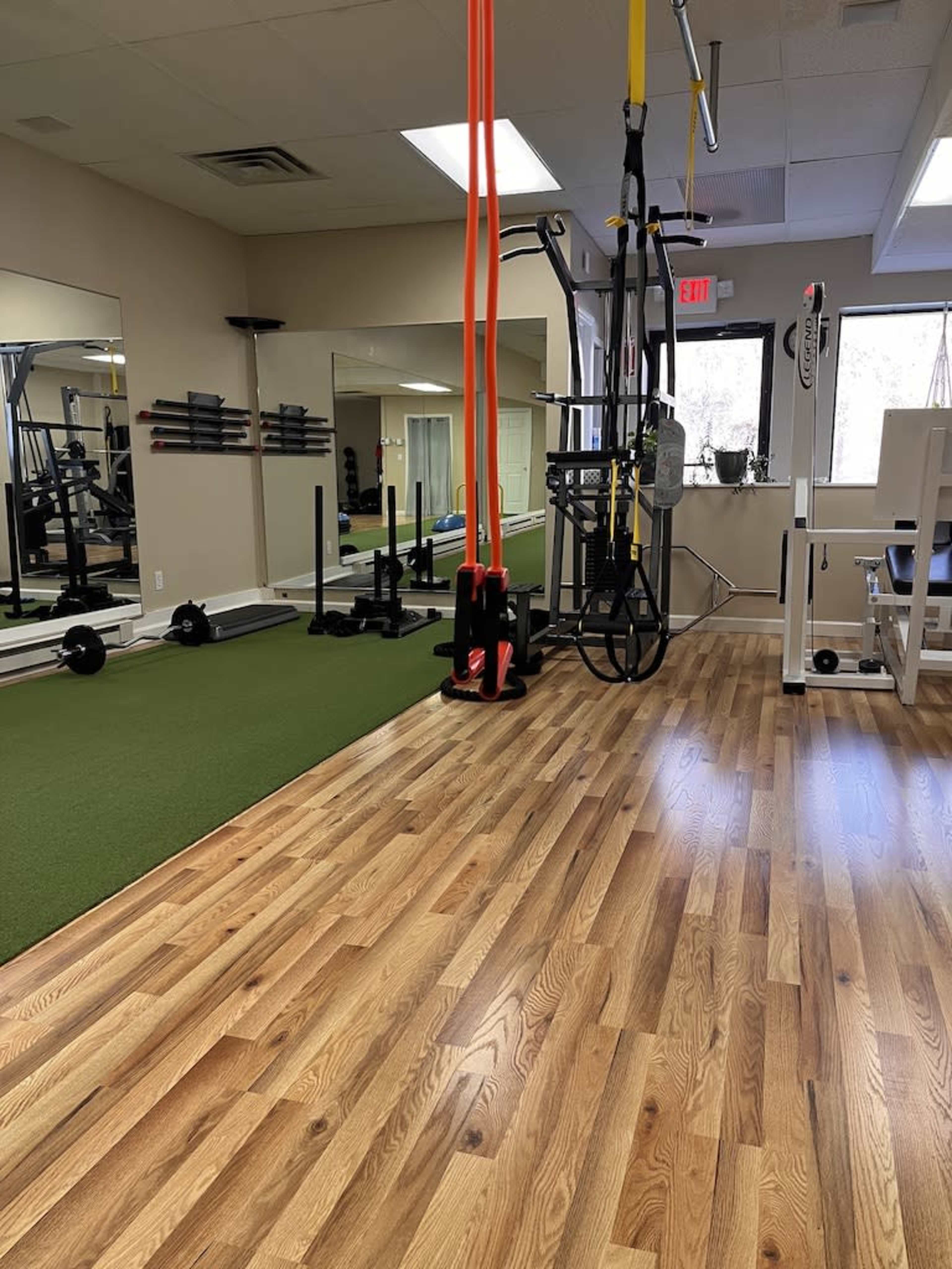 A fitness studio with exercise equipment, including weights and suspension straps, and a section of green turf flooring.