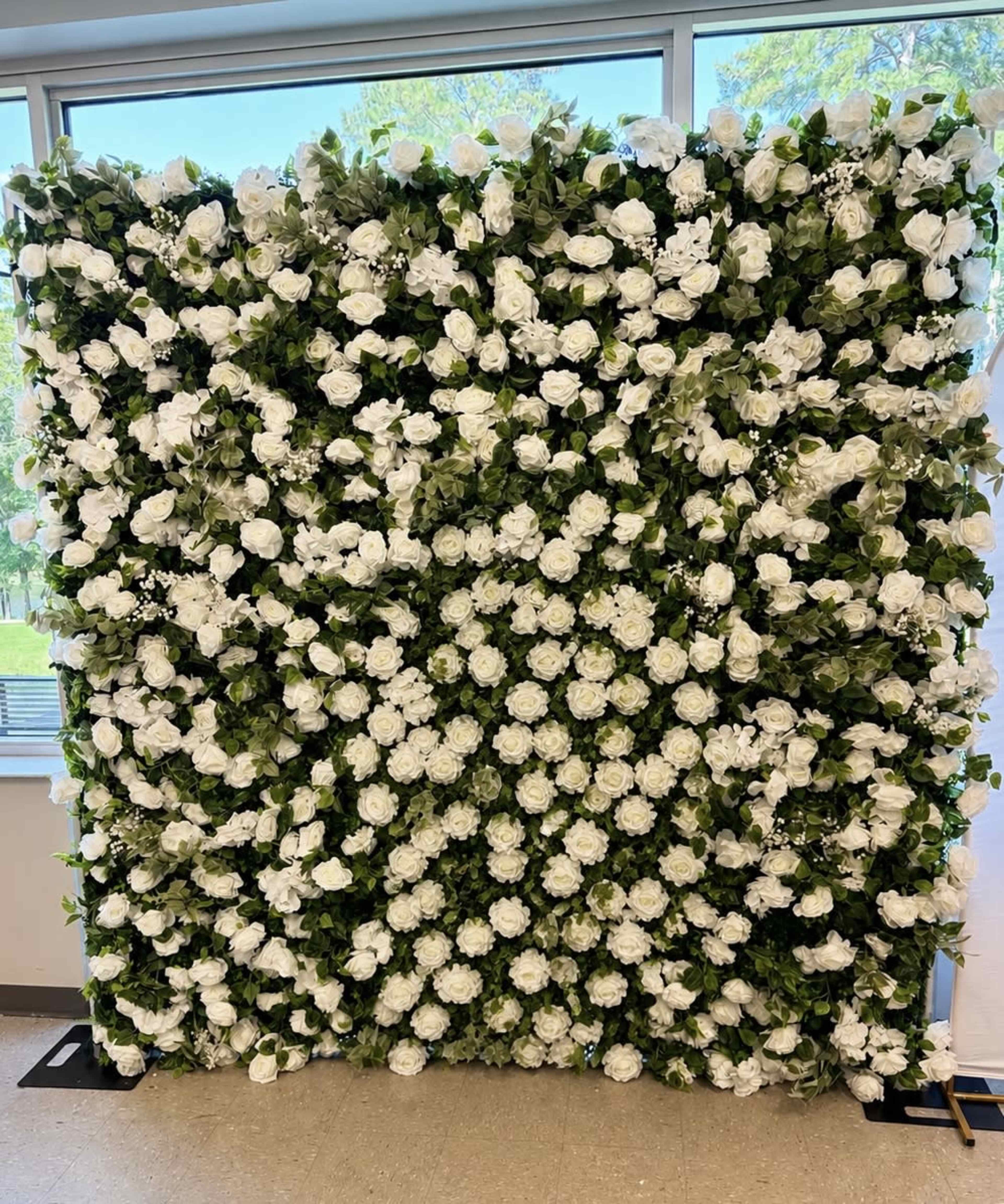 The image depicts a large, rectangular floral wall covered with an abundance of white flowers and green leaves.