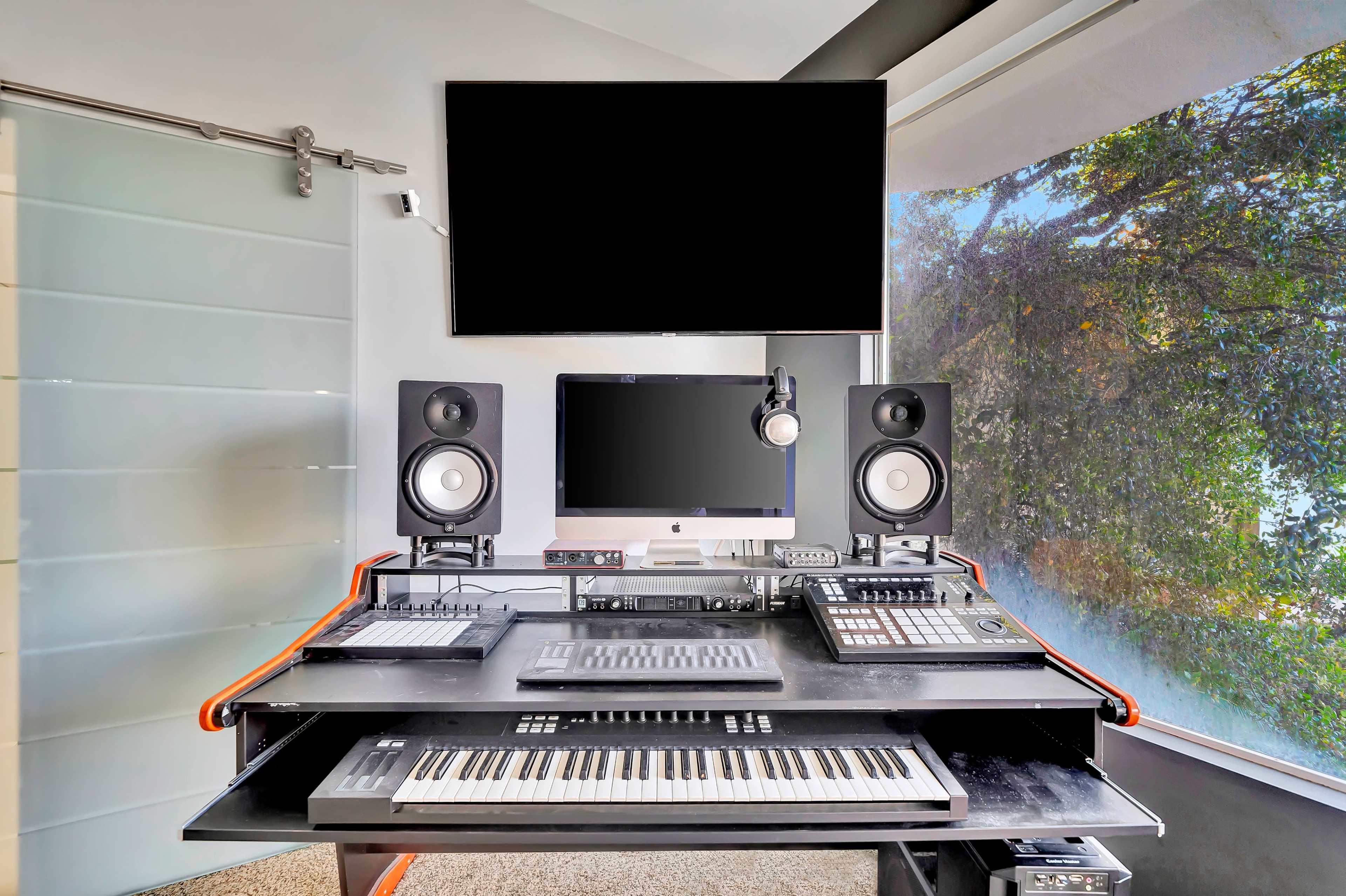 A modern music production studio featuring a keyboard, computer, audio monitors, and a large monitor on a sleek black desk.