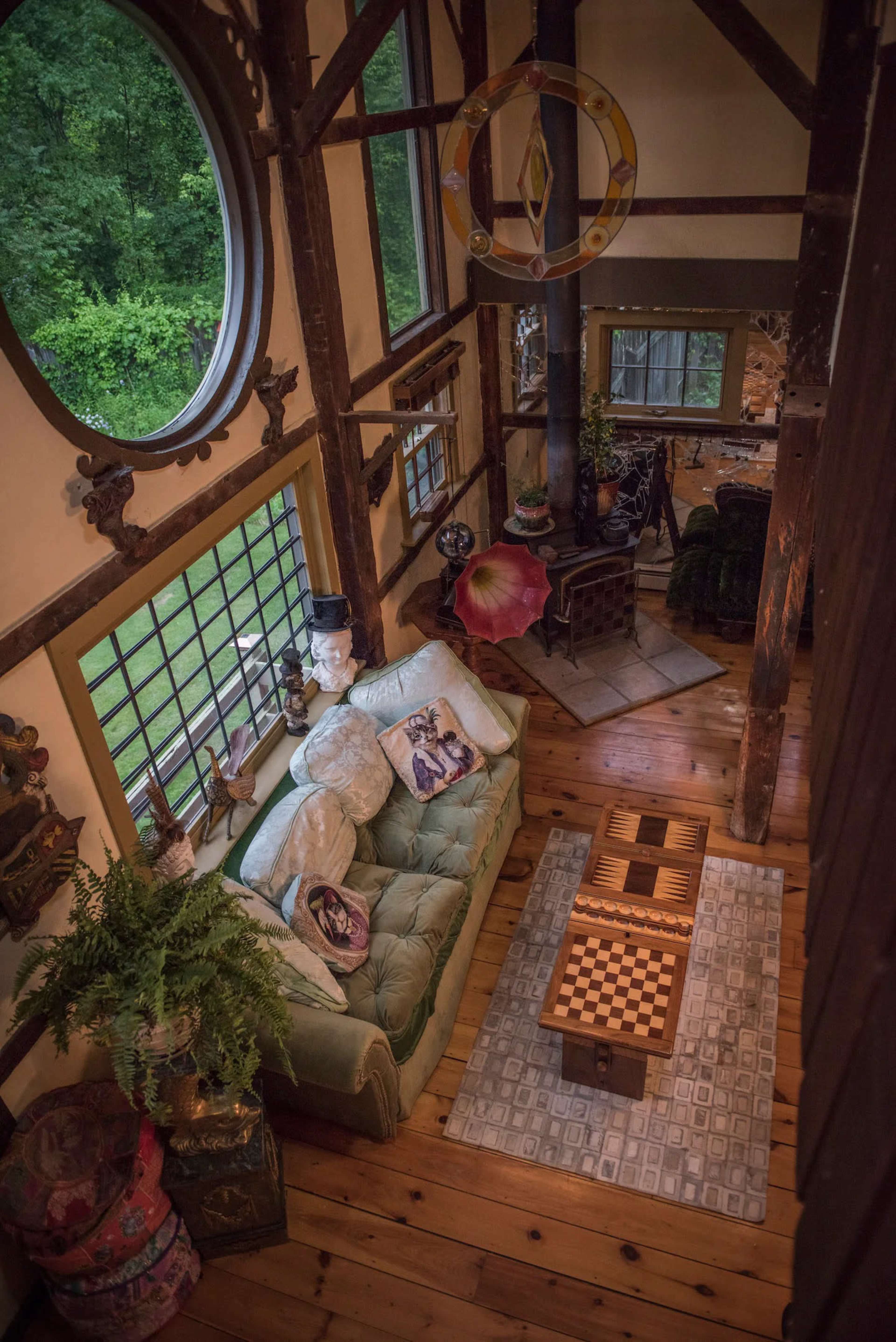 The image shows a cozy interior of a cabin, featuring a green sofa, a wooden coffee table with a checkerboard design, and large windows that provide a view of the outdoors.