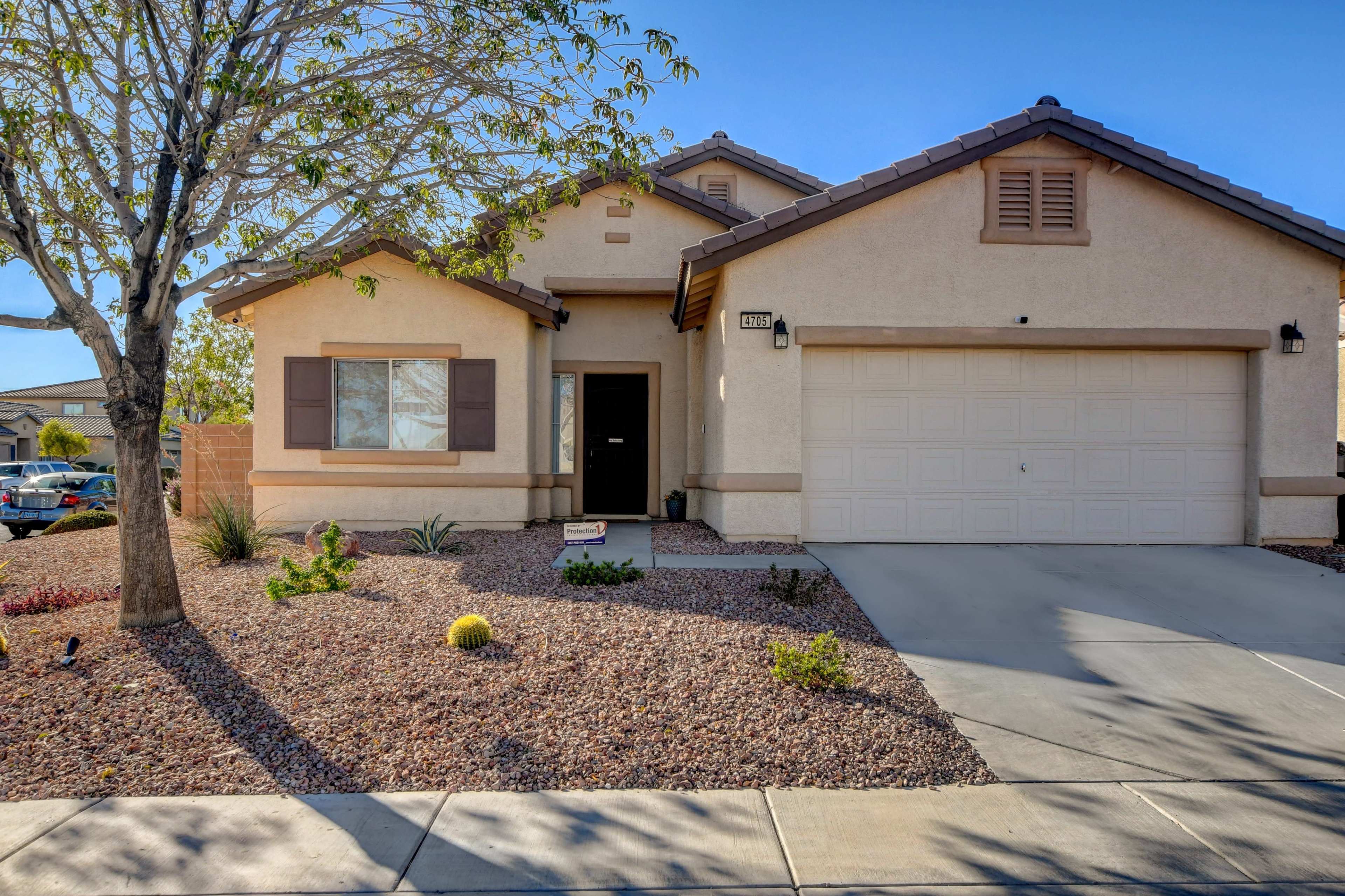 A single-story house with a two-car garage, surrounded by gravel landscaping and a few shrubs.