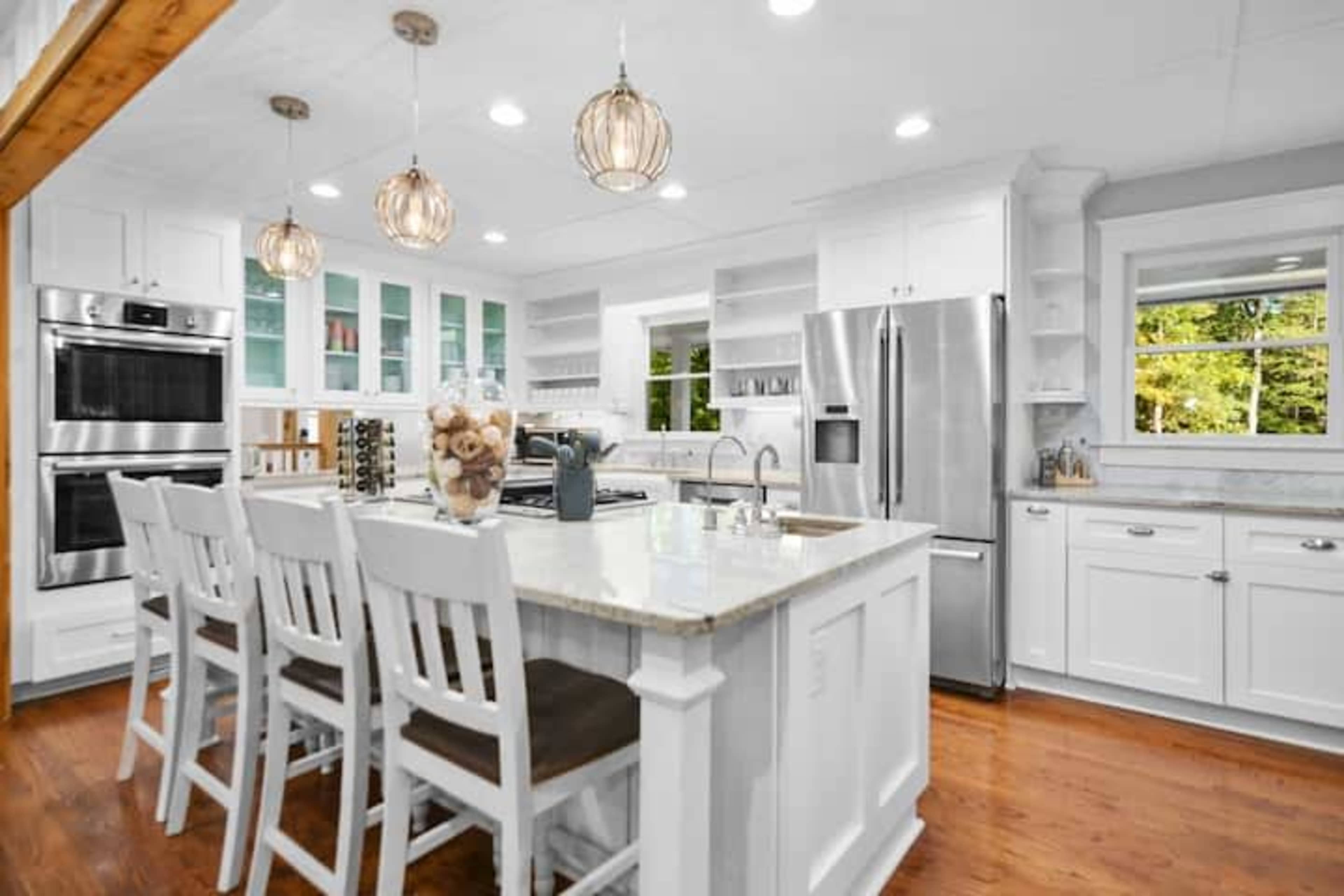 A bright kitchen features white cabinetry, stainless steel appliances, and an island with seating for six.