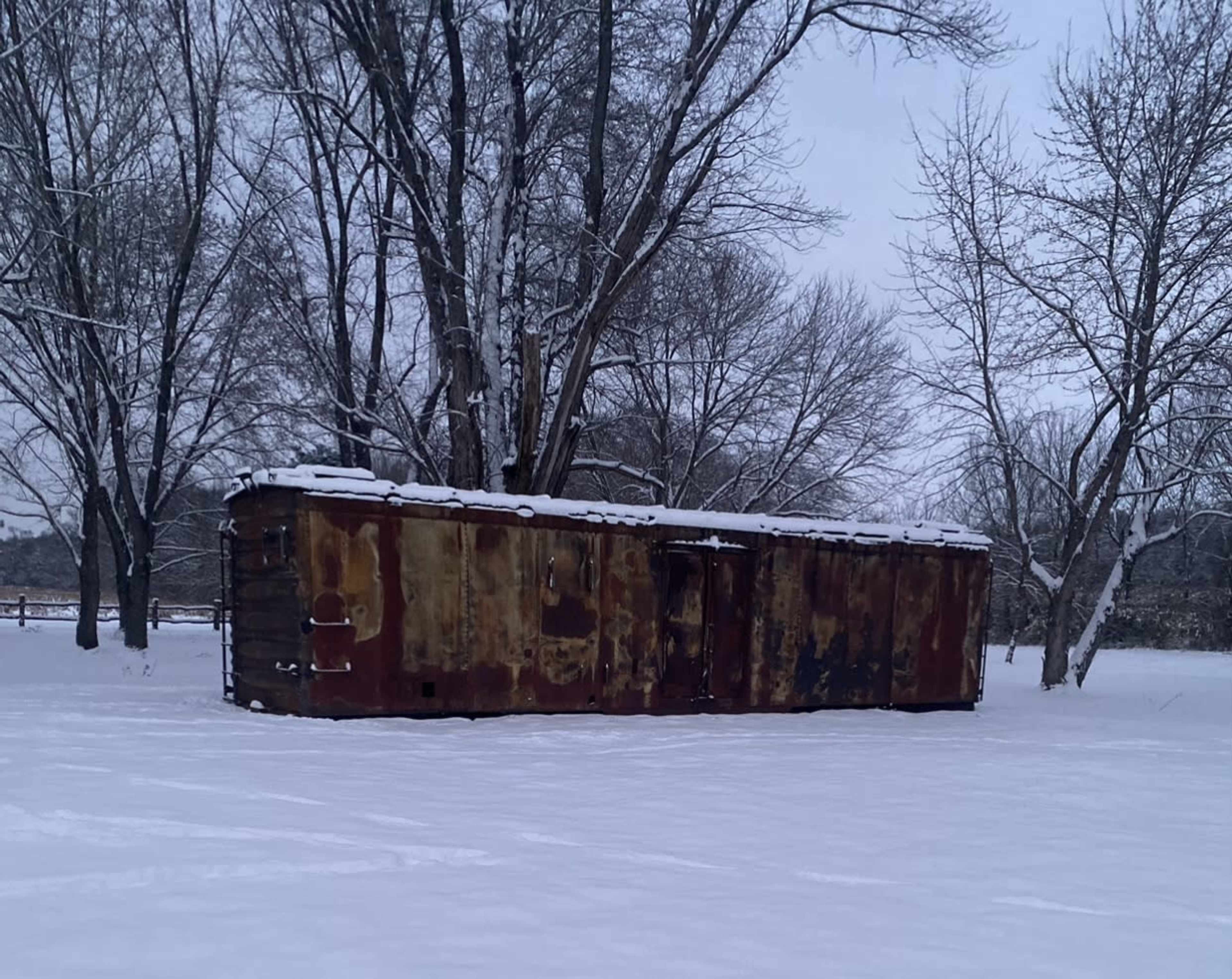 A dilapidated, rusted structure sits surrounded by snow-covered ground and bare trees.