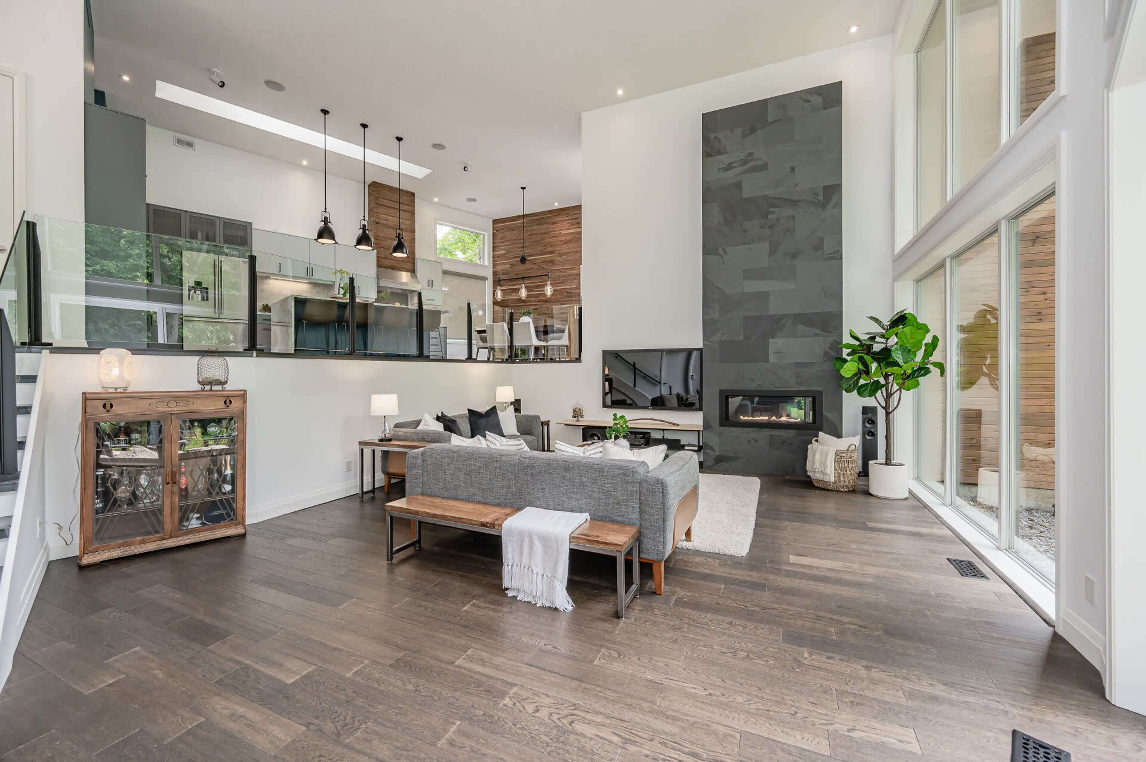 A modern living room with large windows, a sleek fireplace, and a glass partition separating it from a contemporary kitchen.