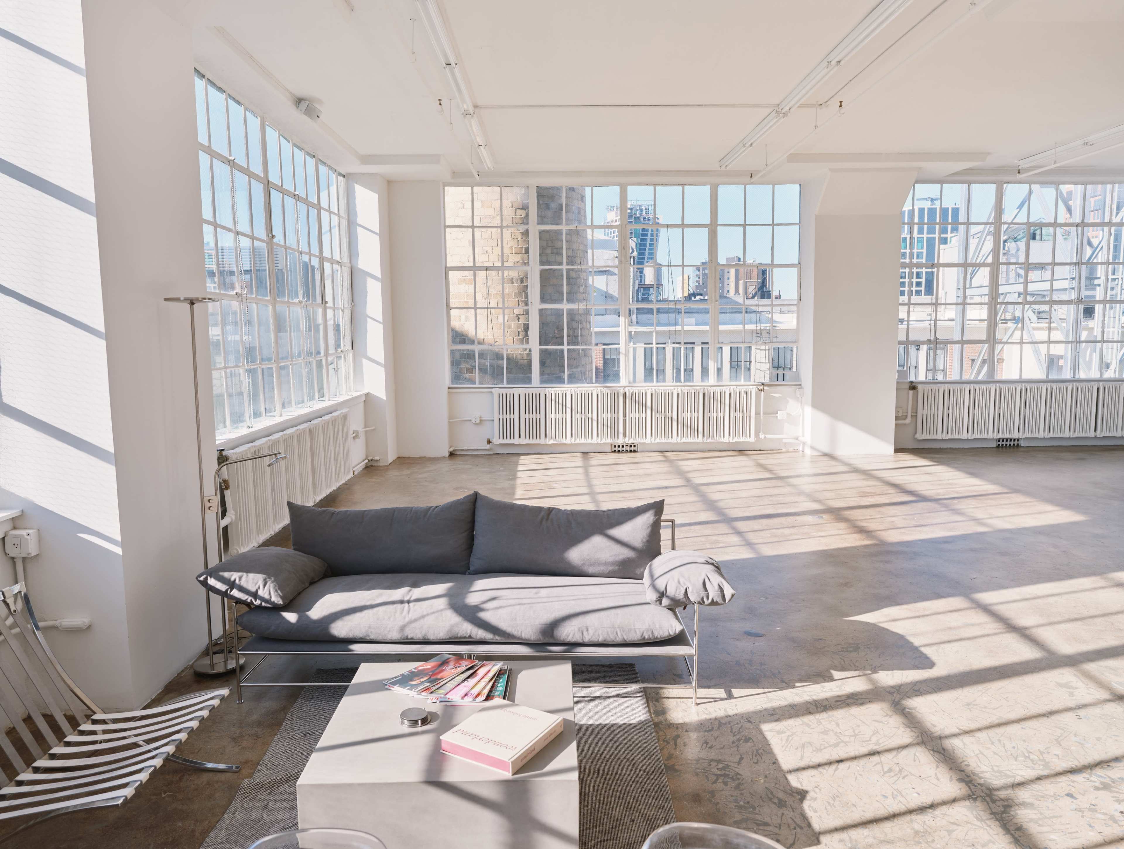 A spacious, brightly lit interior with large windows, featuring a gray sofa and a coffee table with books.