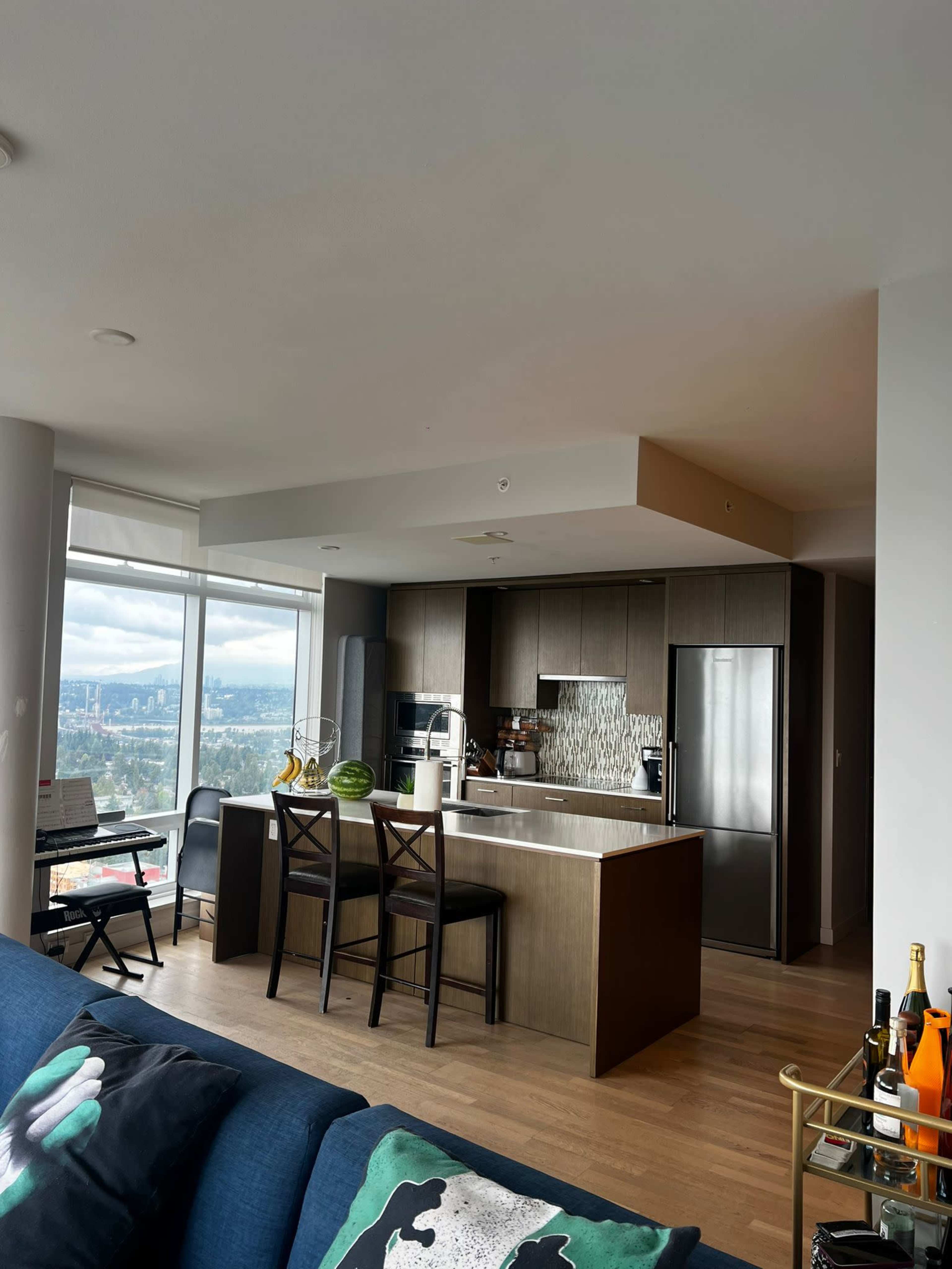 A modern kitchen features dark cabinetry, a large island, and a view of the city through a floor-to-ceiling window.