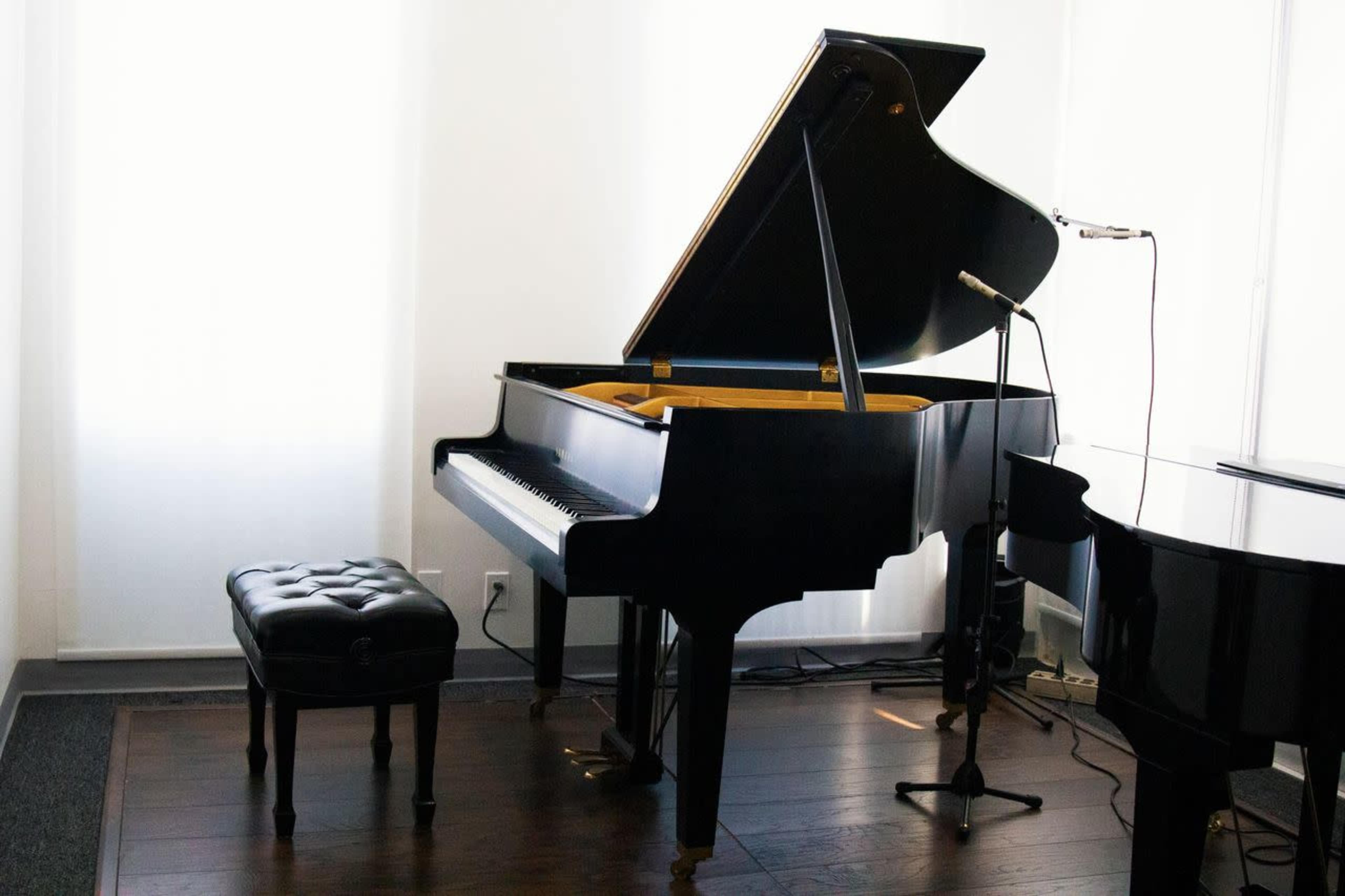 A black grand piano is positioned next to a microphone on a stand in a well-lit room with white walls.