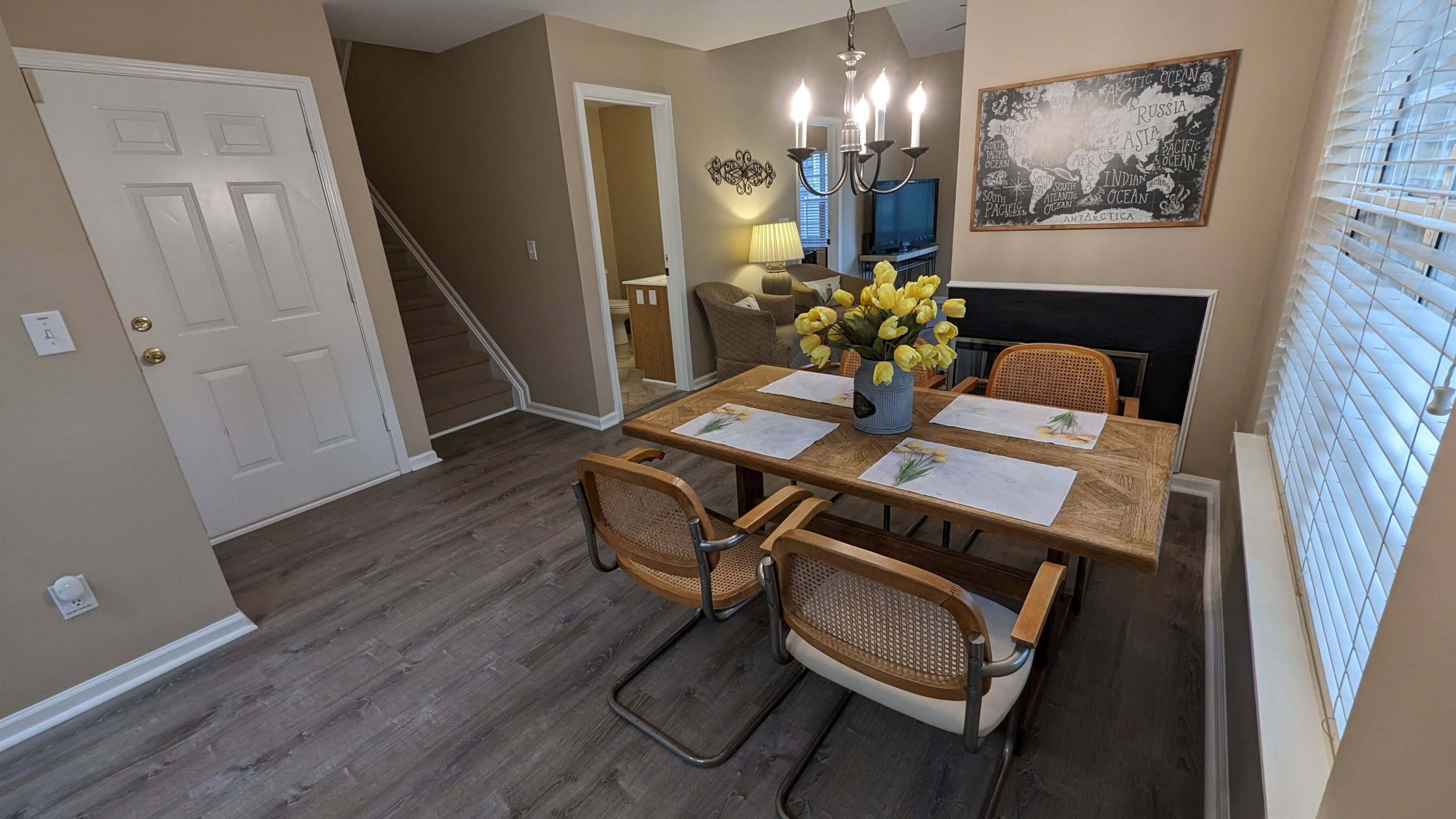 A dining area featuring a wooden table with chairs, a vase of yellow flowers, and a staircase leading to another level.