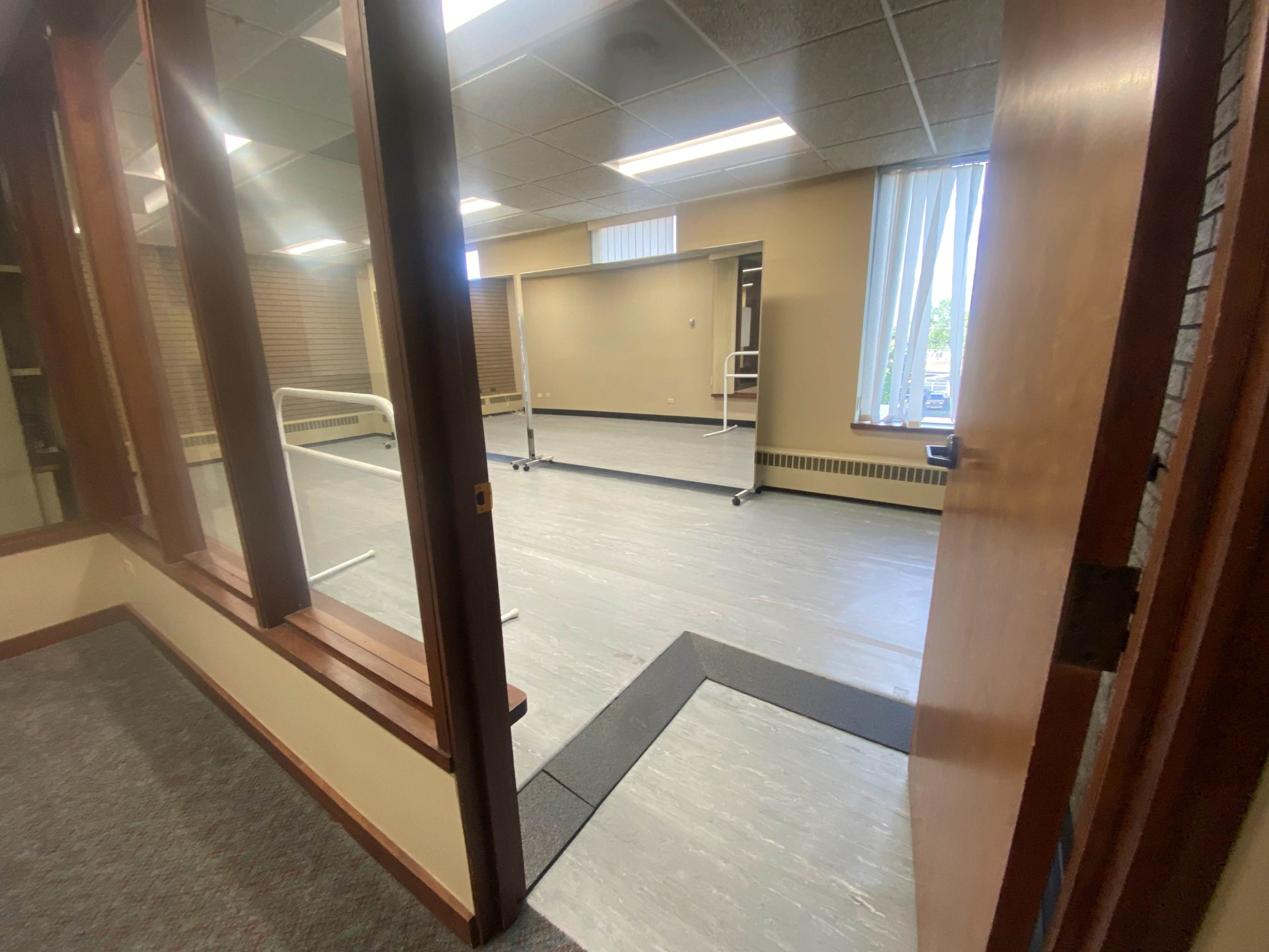 An open doorway leading into a brightly lit dance studio with mirrored walls and wooden ballet bars.