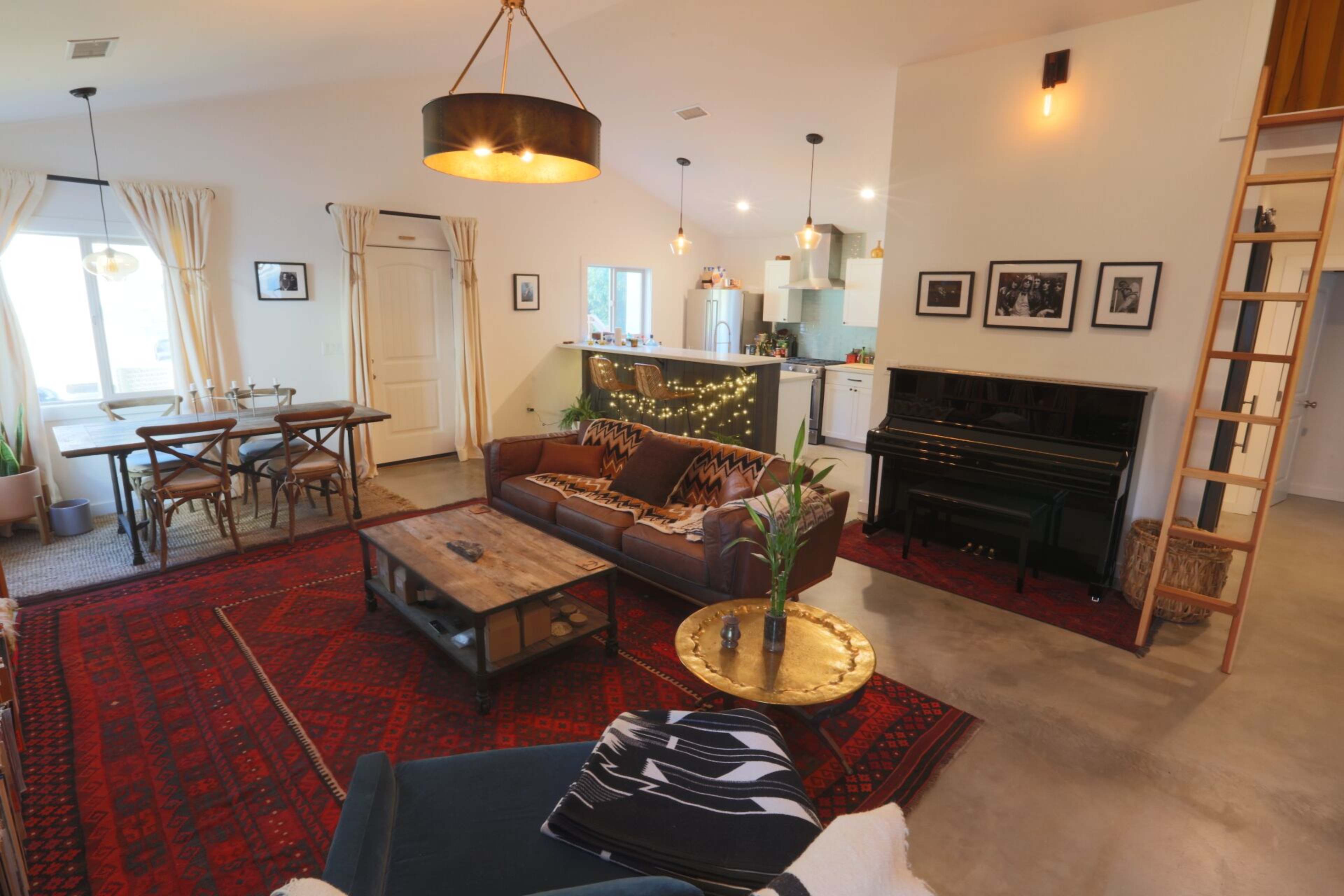 A cozy living space featuring a leather sofa, a wooden coffee table, and a grand piano, all set against a backdrop of an open kitchen and dining area.